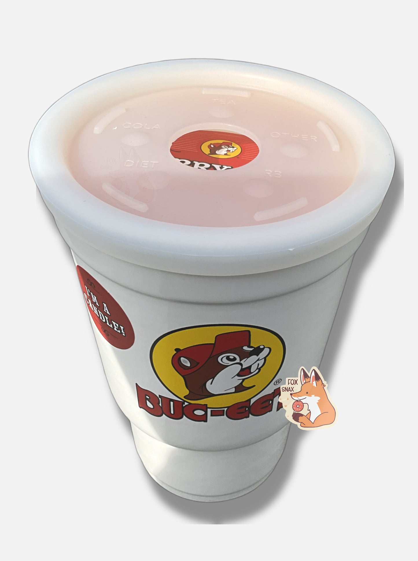 A three-quarters view of the top and front  a large white ceramic candle holder, made to look exactly like a Buc-ee's stryofoam drink cup.  The surface of the cup has the Buc-ee's logo: a cheerful brown-furred beaver with a massive overbite, wearing a ball cap, and underneath it in red text, BUC-EE'S.  The top of the candle is a flexible rubbery material, made to look like the top of a normal cup, and has a hole in the middle for the candle wick.
