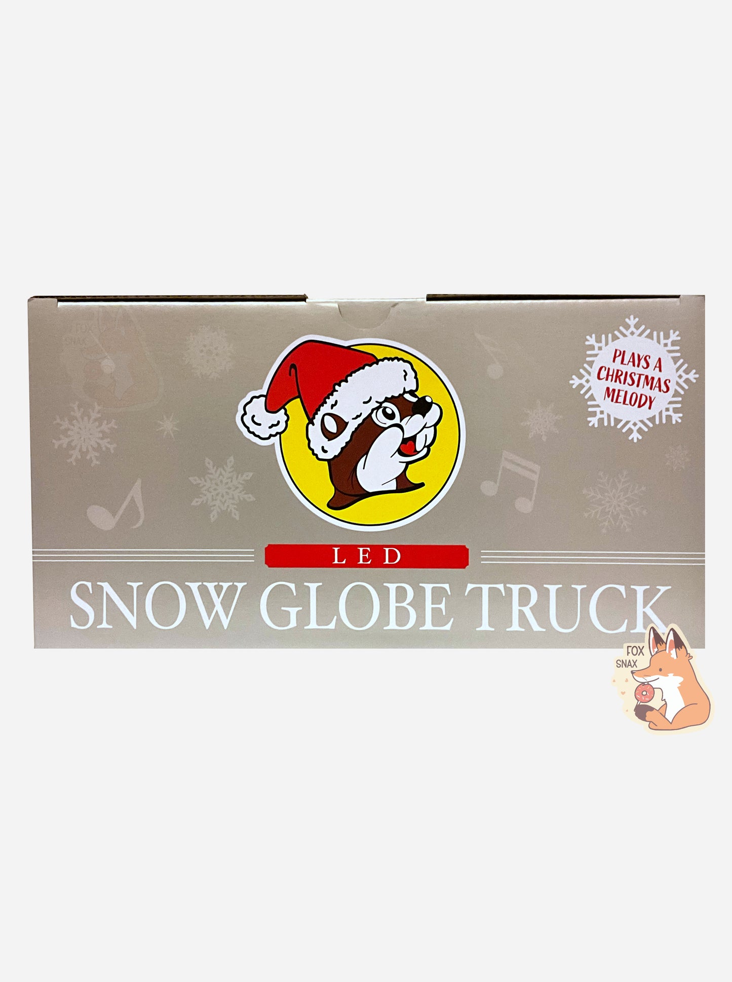 A picture of the top of a grey rectangular box containing Buc-ee's Led Snow Globe Truck.  The top has the Buc-ee's logo - a cartoon beaver wearing a Santa hat.  A snowflake in the background reads PLAYS A CHRISTMAS MELODY.