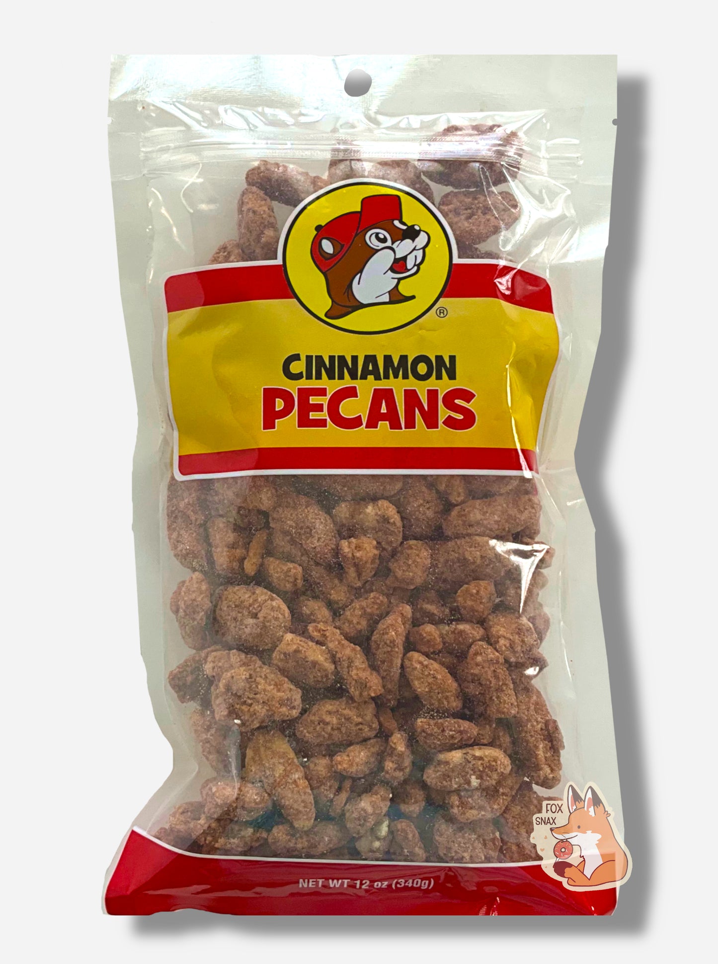 A picture of a clear plastic bag of Buc-ee's Cinnamon Pecans.  The Buc-ee's logo can be seen in the top center of the bag, then underneath that in black and red text, CINNAMON PECANS.  The bottom of the bag is red and reads Net Wt 12 oz.  Inside the bag are a large number of dried pecans, covered in brownish, reddish sugary cinnamon coating.