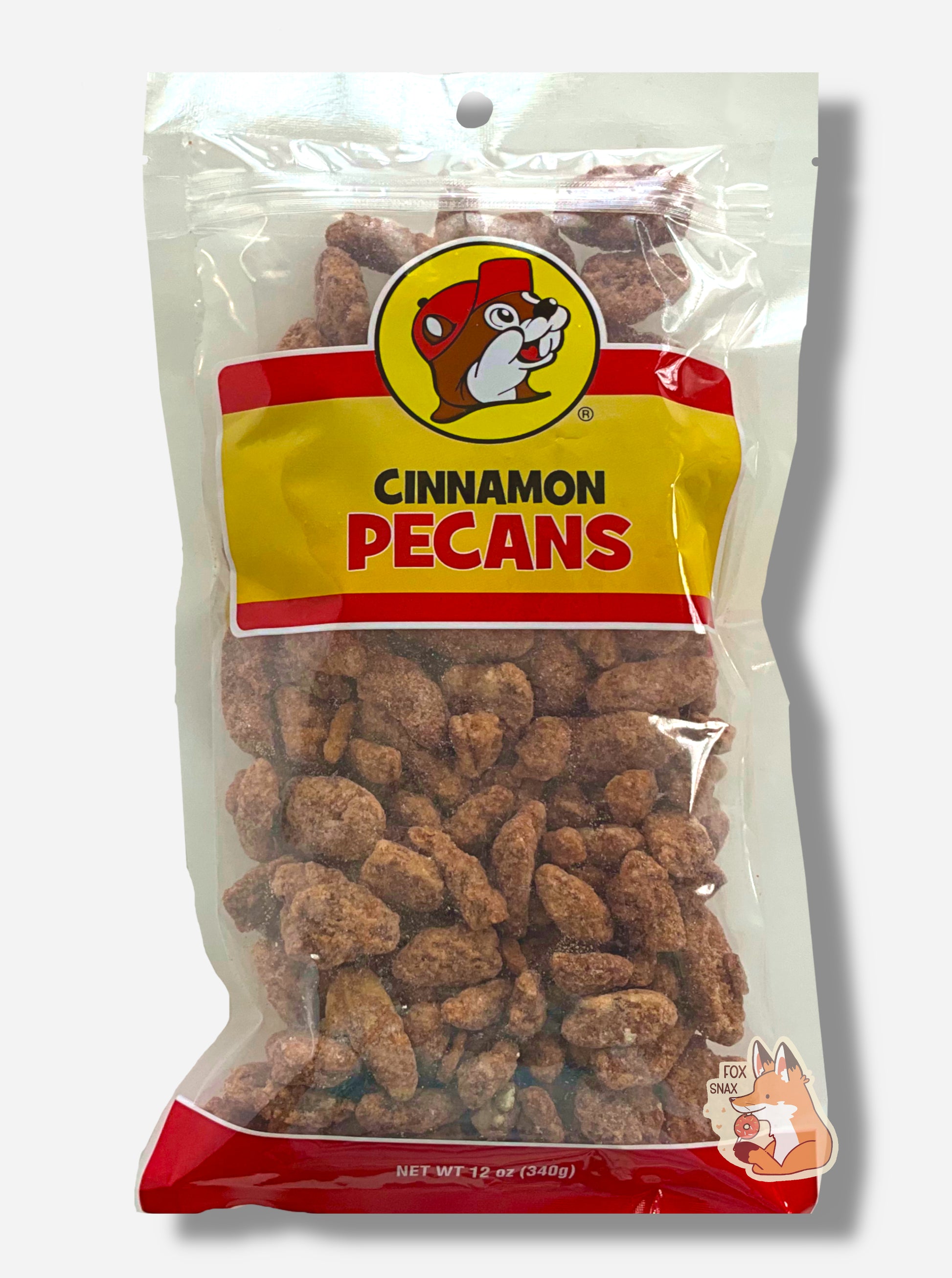 A picture of a clear plastic bag of Buc-ee's Cinnamon Pecans.  The Buc-ee's logo can be seen in the top center of the bag, then underneath that in black and red text, CINNAMON PECANS.  The bottom of the bag is red and reads Net Wt 12 oz.  Inside the bag are a large number of dried pecans, covered in brownish, reddish sugary cinnamon coating.