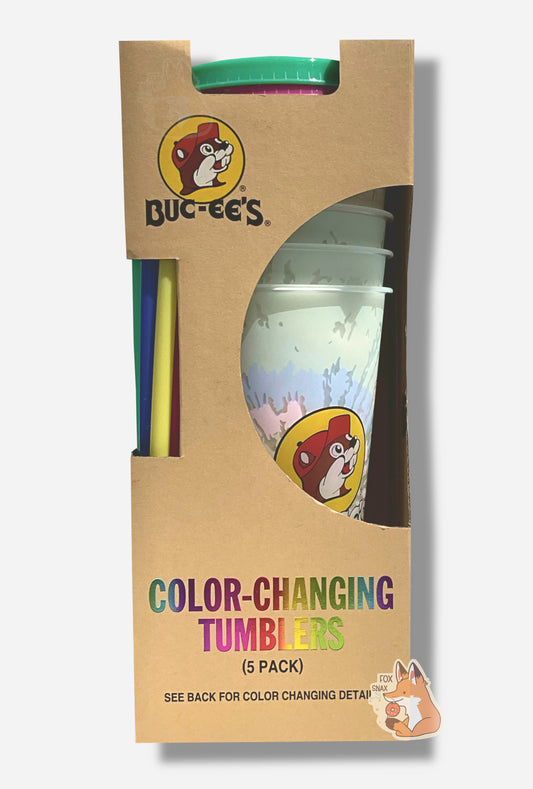 A picture of a tall, thin cardbox box.  The bottom of the box reads COLOR-CHANGING TUMBLERS.  The top  of the box has the Buc-ee's logo.  In the middle is a semicircle cut out, which exposes the plastic tumblers.  Several tumblers can be seen, and they show a faded, white-ish plastic tumbler with a faint tie-dye pattern through the semicircle.  Each of the tumblers is tall, plastic, and has the Buc-ee's logo on it.