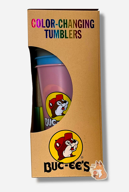 A picture of a tall, thin cardbox box.  The top of the box reads COLOR-CHANGING TUMBLERS.  The bottom of the box has the Buc-ee's logo.  In the middle is a semicircle cut out, which exposes the plastic tumblers.  A "bubble gum" and "sky" plastic tumbler can be seen through the semicircle.  Each of the tumblers is tall, plastic, and has the Buc-ee's logo on it.