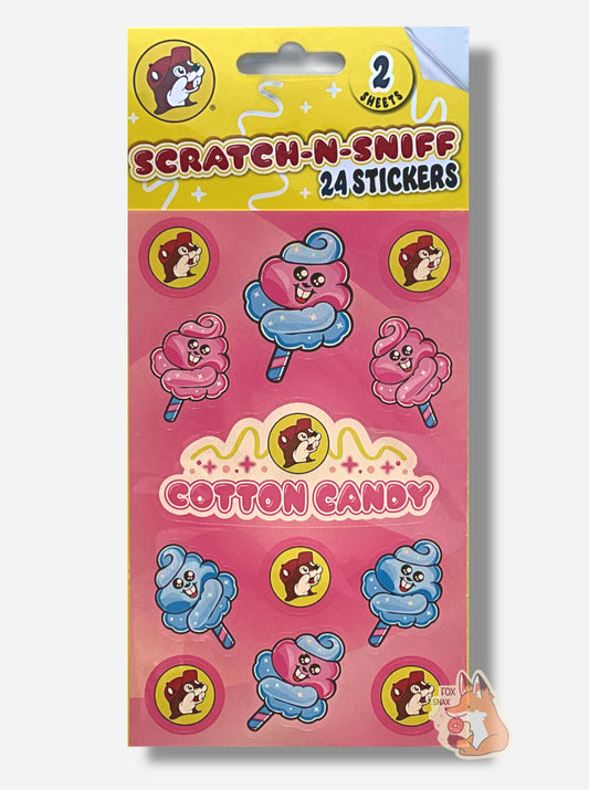 A rectangular package of Buc-ee's Scratch-N-Sniff Cotton Candy stickers.  The stickers on the package are the Buc-ee's logo - a brown-furred beaver with a massive overbite, pink cotton candy puffs with a beaver grin on its body, blue cotton candy puffs with a beaver grin on its body, a larger pink/blue puff with a beaver grin (it's all a bit surreal), and in the middle, a Buc-ee's logo with the words COTTON CANDY.  The top of the package reads 2 SHEETS, then SCRATCH-N-SNIFF, 24 STICKERS