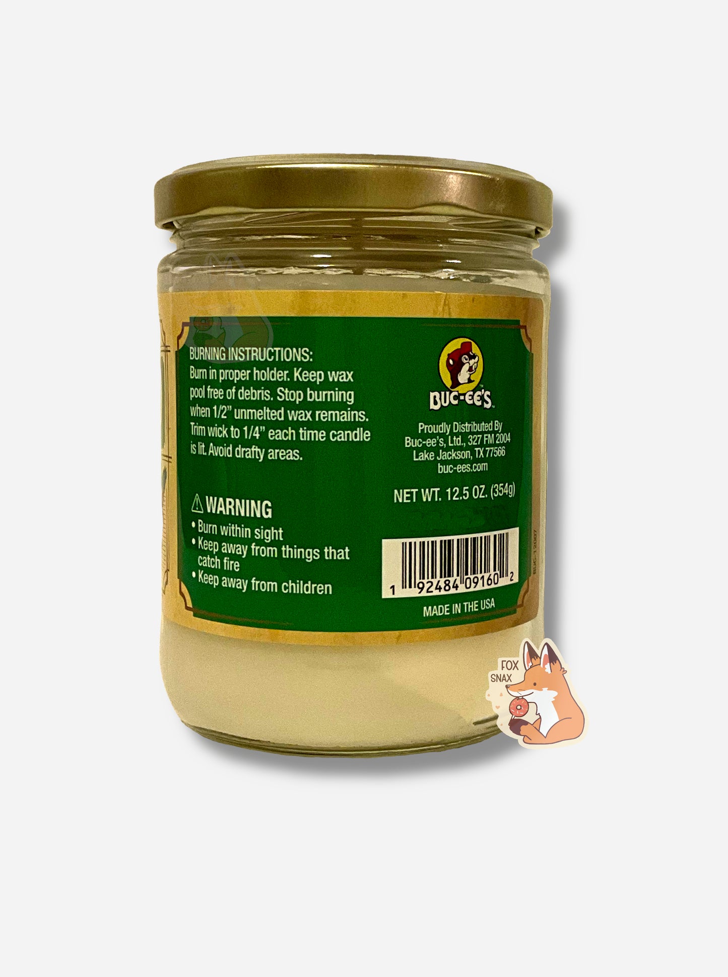 A picture of a white/yellow candle in a cylindrical glass container.  The lid of the container is a gold colored metal lid.  The text on a green sticker on the back reads BURNING INSTRUCTIONS: Burn in proper holder. Keep wax pool free of debris. Stop burning when 1/2" unmelted wax remains. Trim wick to 1/4" each time candle is lit.  Avoid drafty areas.  Net Wt 12.5 Oz.  MADE IN THE USA