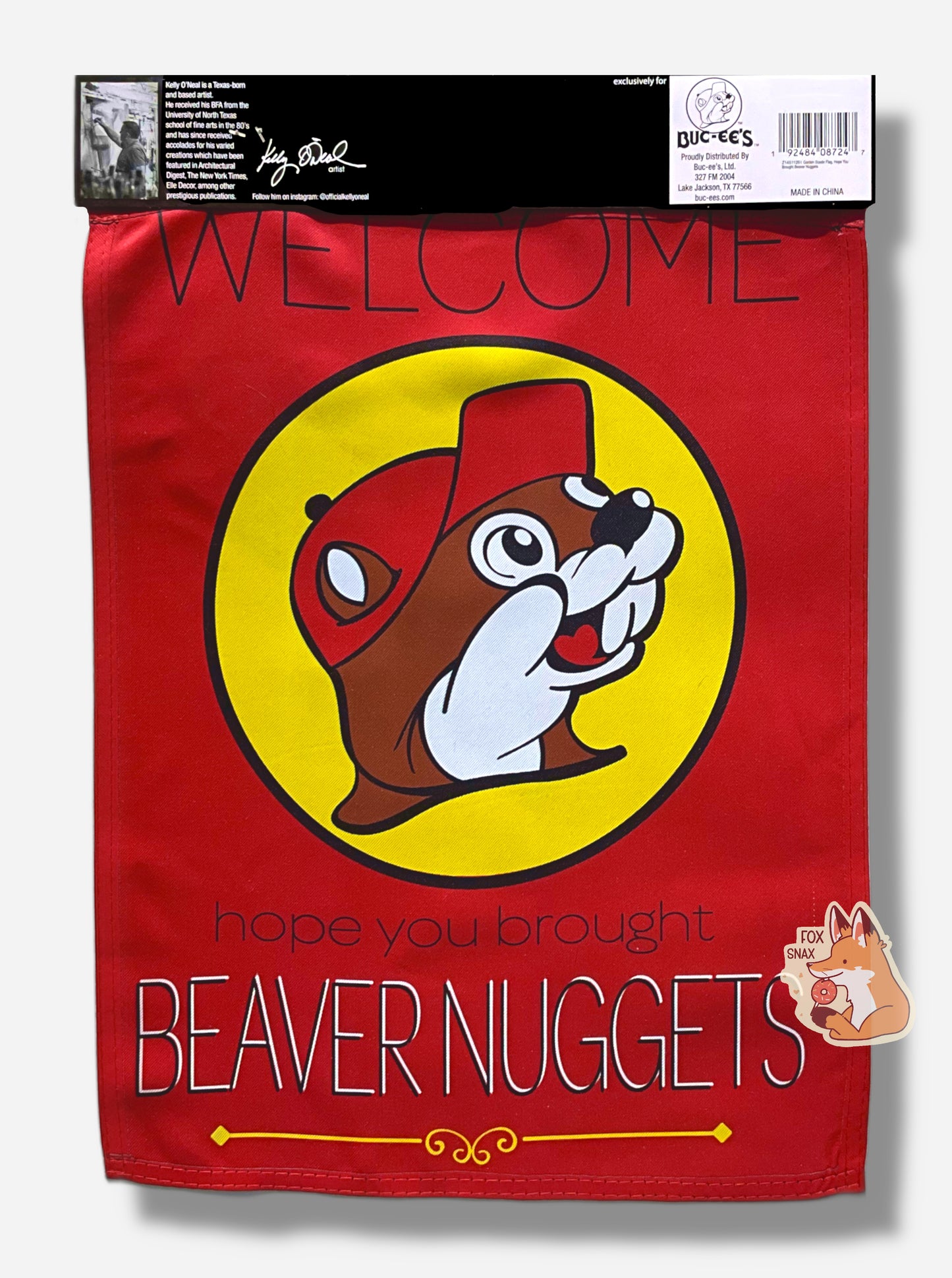 A picture of the back of a pretty red garden flag.  It is the same as the front;t he flag has a  Buc-ee's logo dead in the center - a cheerful beaver with an overbite, wearing a red cap, framed by a yellow circle.  The top of the flag reads WELCOME in thin uppercase black text.  The bottom of the flag reads "hope you brought" in lowercase black text, then "BEAVER NUGGETS" in white/black uppercase text.  The top of the flag has a bit of paper on it, part of the wrapping (not flag), that reads GARDEN FLAG/