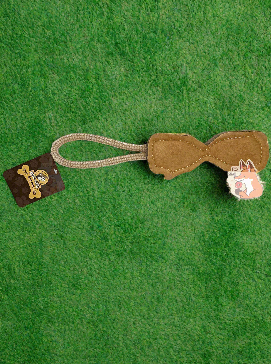 A close up picture the back of a Buc-ee's "Pet Essentials" Log Rope dog toy.  The body of the toy is shaped like a log - roughly - with a flat body and a dip in the middle, presumably to make it easier for a dog to bite it.  On one end is a strong tan rope.  The body of the tool is tan, Both ends of the  rope are tied into one end of the "log", making a loop for a person to hold on to.  The background is of fuzzy green artificial grass.