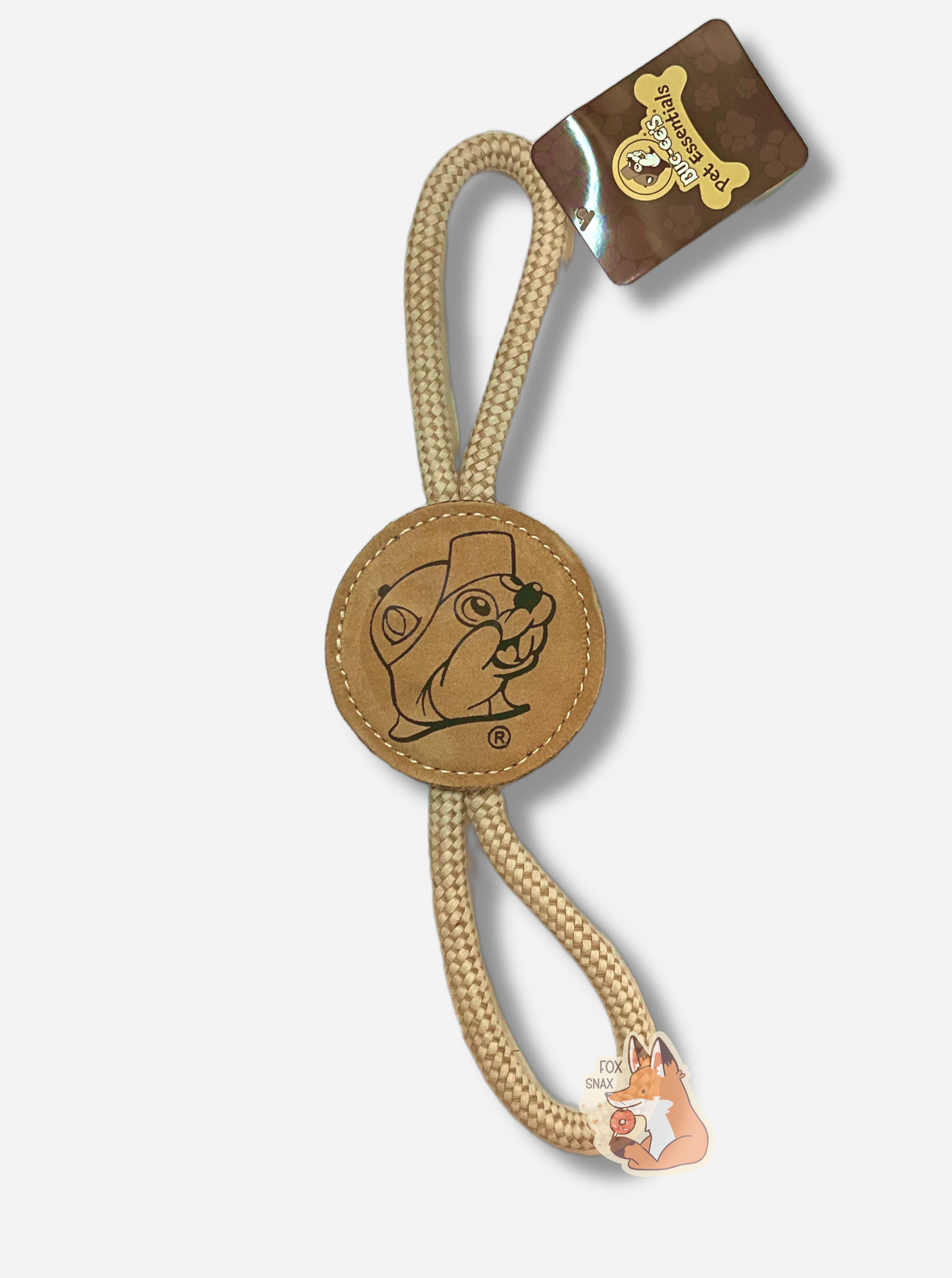 A picture of a Buc-ee's "Pet Essentials" Natural Disc dog toy.  The body of the toy is shaped like a circle - made of a material allowing a dog, if they so chose, to bite it.  On both ends are strong tan ropes that form a loop back to the body of the circl  The body of the tool is tan, and also has a black outline of Buc-ee The Beaver.  The ends of the  rope are tied into one end of the "log", making a loop for a person (or dog) to hold on to.  A brown rectangular tag says BUC-EE'S PET ESSENTIALS.