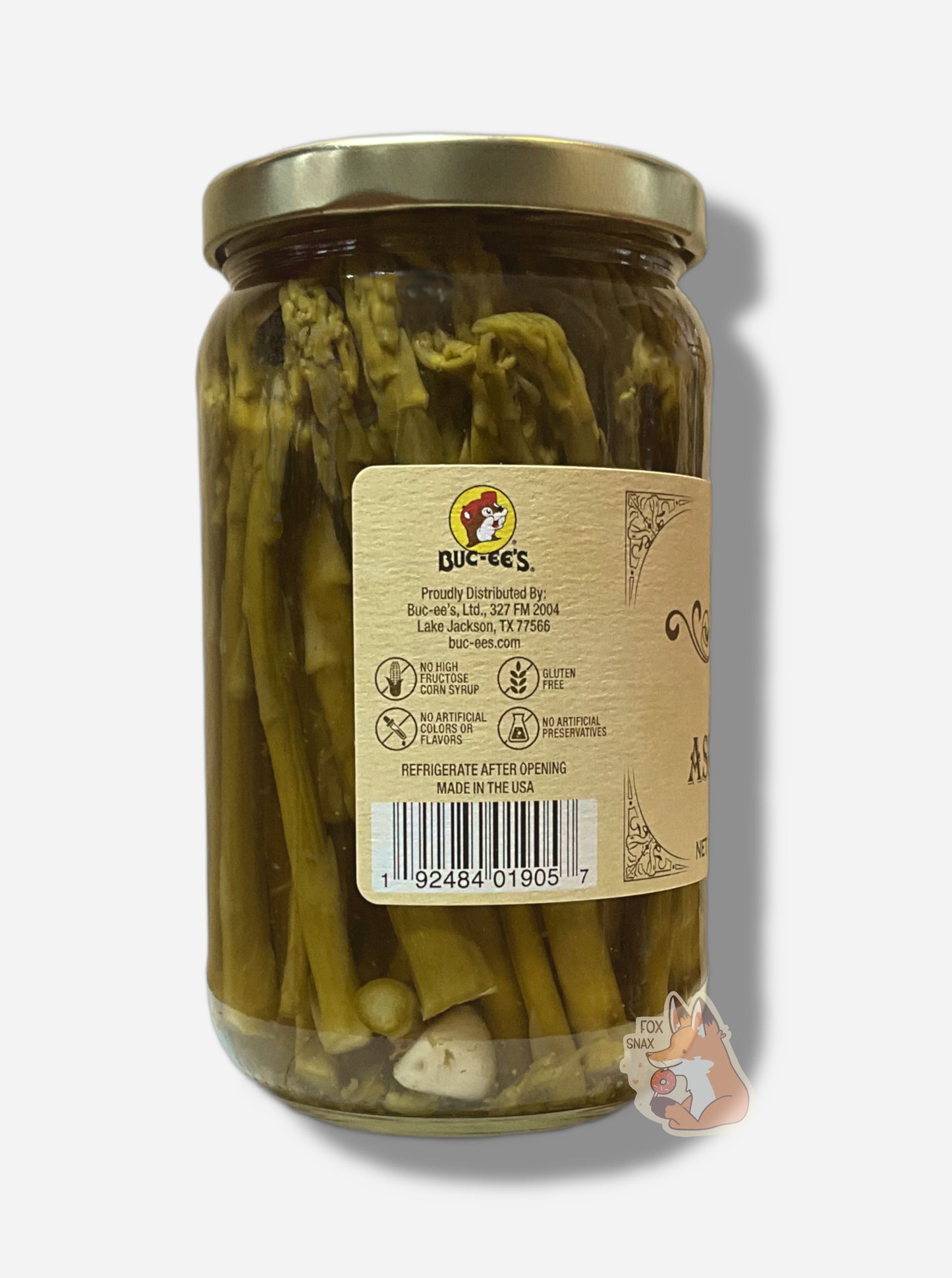 A picture of the left side of a glass jar of Buc-ee's Pickled Asparagus - the label is a "old-timey" sort of white/yellow with flared edges.  The middle reads No High Fructose Corn Syrup, No Artificial Colors Or Flavors, Gluten Free. In the jar, long dark asparagus spears can be seen, interspersed with white garlic cloves. 