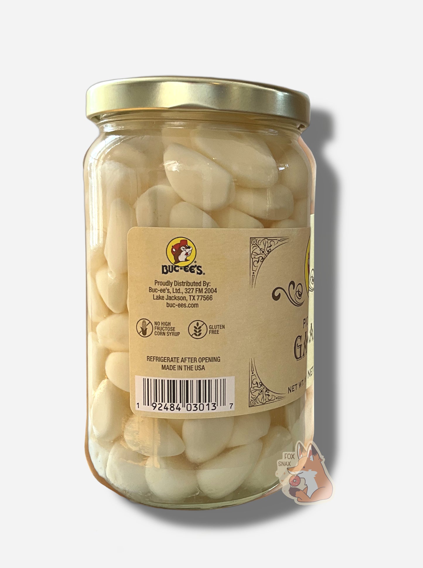 A picture of the left side of a glass jar of Buc-ee's Pickled Garlic - the label is a "old-timey" sort of white/yellow with flared edges.  The middle reads No High Fructose Corn Syrup, Gluten Free. In the jar, garlic gloves floating in clear brine can be seen.