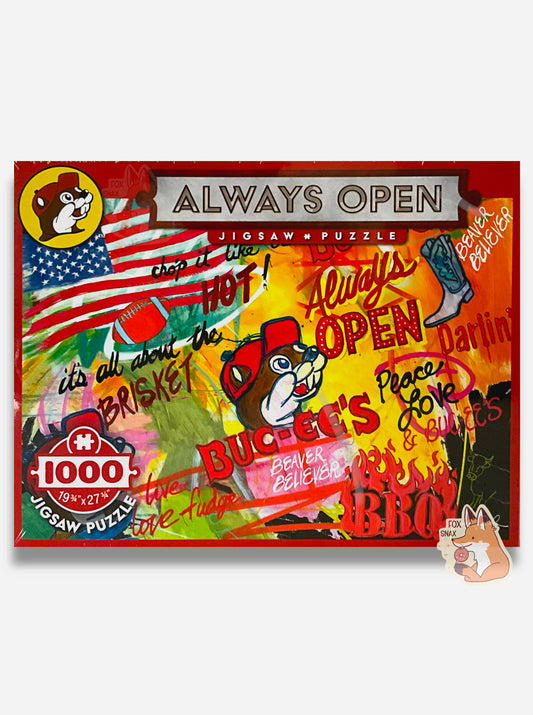 A picture of an extremely colorful puzzle.  The top of the puzzle reads ALWAYS OPEN, then JIGSAW PUZZLE in smaller font.  The lower left reads 1000 (pieces), 19 3/4 x 27 3/4.  The top left has the Buc-ee's logo.  The puzzle itself is a collage of different painted items: the Buc-ee's logo, an American flag, a red football, a cowboy boot, and the following words, each in a different colorful font: IT'S ALL ABOUT THE BRISKET, CHOP IT LIKE IT'S HOT, ALWAYS OPEN, PEACE, LOVE & BUCEE'S, BEAVER BELIEVER, BBQ