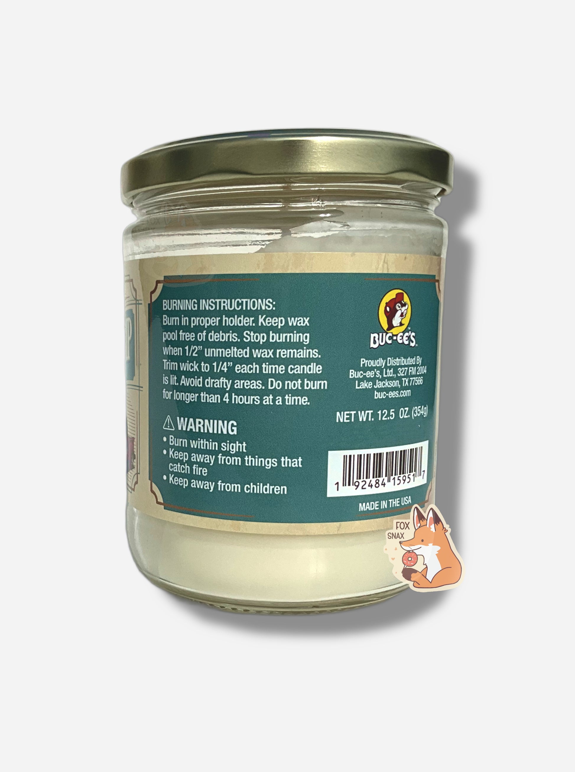 A picture of a white/yellow candle in a cylindrical glass container.  The lid of the container is a light gold colored metal lid.  The text on a blue sticker on the back reads BURNING INSTRUCTIONS: Burn in proper holder. Keep wax pool free of debris. Stop burning when 1/2" unmelted wax remains. Trim wick to 1/4" each time candle is lit.  Avoid drafty areas.  Net Wt 12.5 Oz.  MADE IN THE USA
