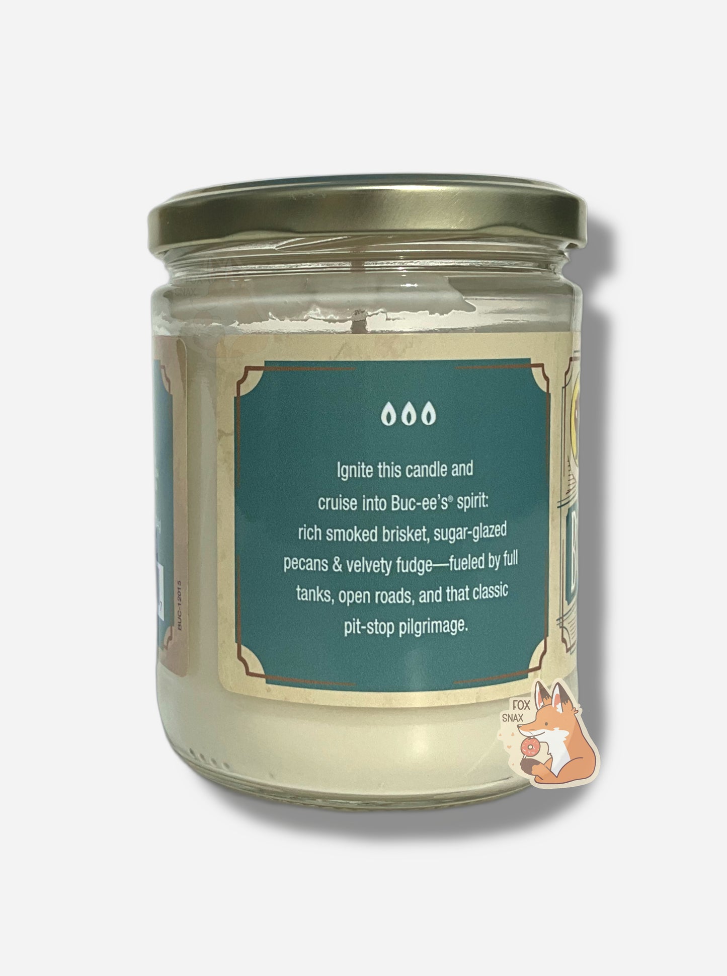 The back of a Buc-ee's Road Trip candle.  It reads: IGNITE THIS CANDLE AND CRUISE INTO THE BUC-EE'S SPIRIT: RICH SMOKED BRISKET, SUGAR-GLAZED PECANS & VELVETY FUDGE - FUELED BY FULL TANKS, OPEN ROADS, AND THAT CLASS PIT-STOP PILGRIMAGE.  The text is white against a light blue background, and has three images of flames over the top of the text.