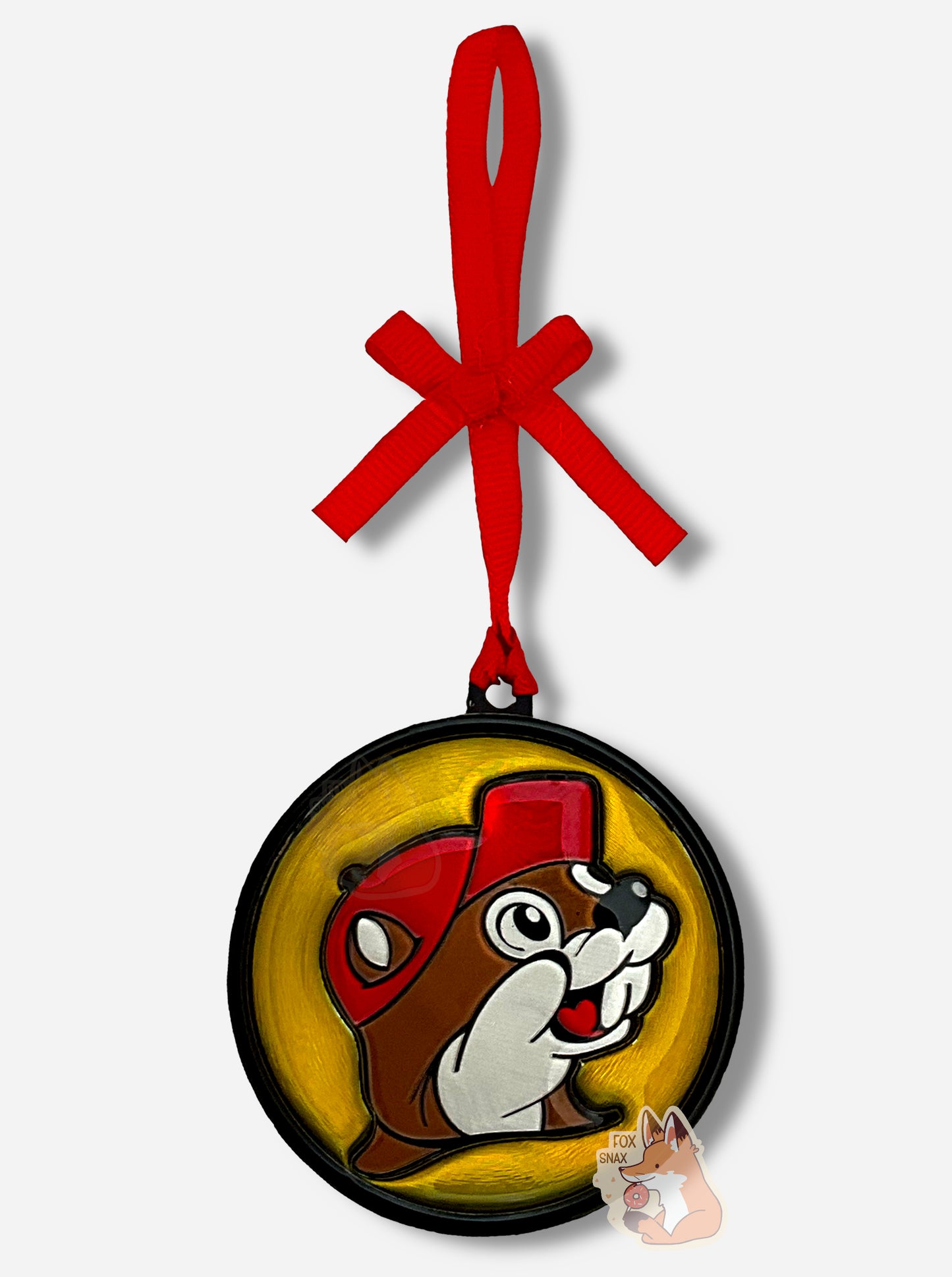 A picture of the front of a round, shiny, Christmas ornament.  The ornament is of the Buc-ee's logo - a smiling beaver wearing a red ballcap.  It is made out of foil and plastic, and is extremely shiny.  A red ribbon pokes out from the top of the ornament's body, and curves upward in a pretty bow.