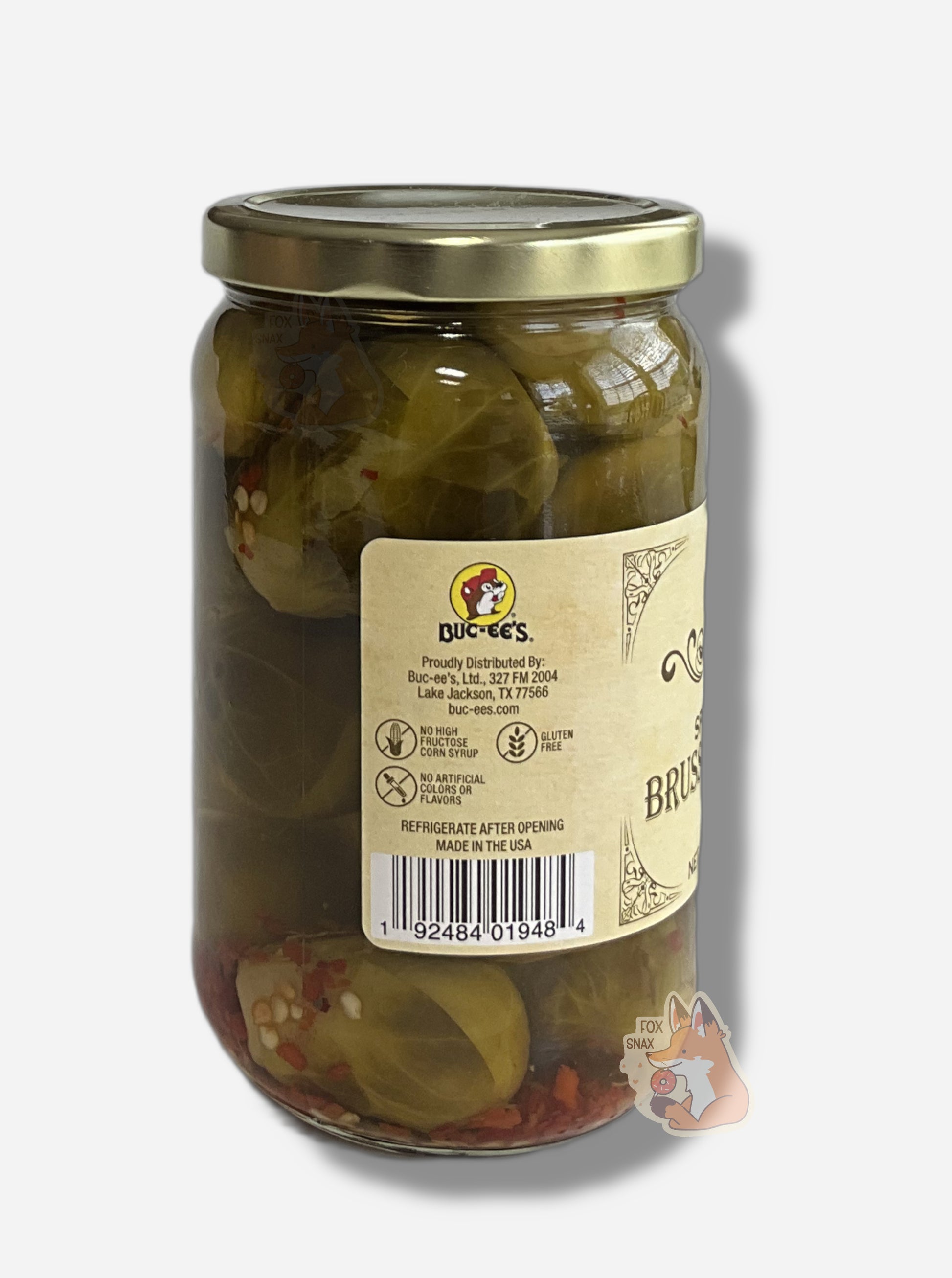 A picture of the left side of a glass jar of Buc-ee's Spicy Pickled Brussels Sprouts - the label is a "old-timey" sort of white/yellow with flared edges.  The middle reads No High Fructose Corn Syrup, No Artificial Colors Or Flavors, Gluten Free. In the jar, floating sprouts in a green brine can be seen, dotted with red pepper flakes throughout.