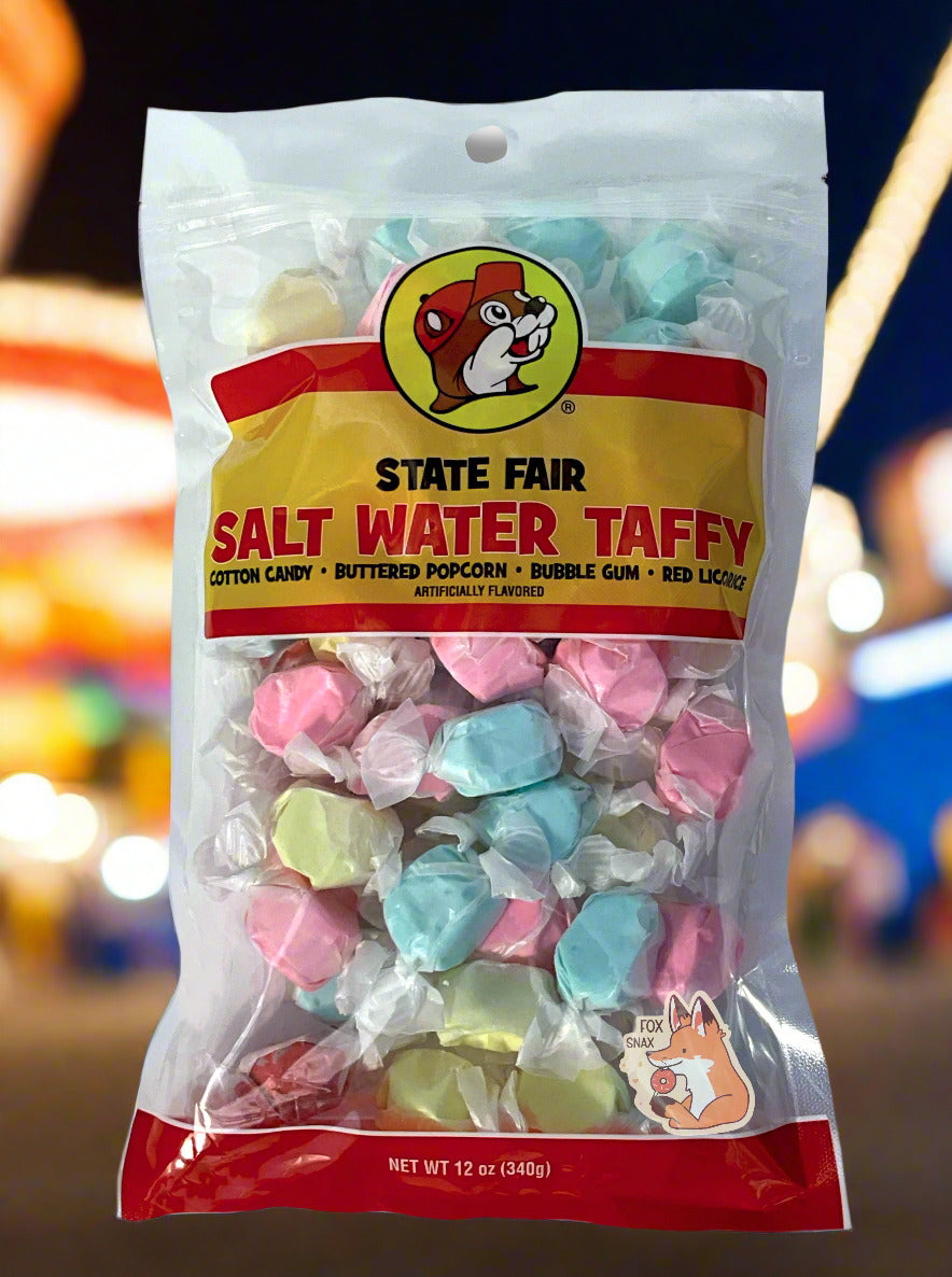A picture of the front of a plastic bag of Buc-ee's State Fair Salt Water Taffy.  The bag is clear plastic with the Buc-ee's logo.  Inside it, twists of candy in four different wrapping colors (cotton candy, buttered popcorn, bubble gum, red licorice) can be seen.  The front of the bag has the Buc-ee's logo - a brown-furred beaver with a significant overbite, wearing a red ball cap - and reads:  STATE FAIR SALT WATER TAFFY, ARTIFICIALLY FLAVORED, then 12 OZ.  Bright colorful lights are seen behind the bag.