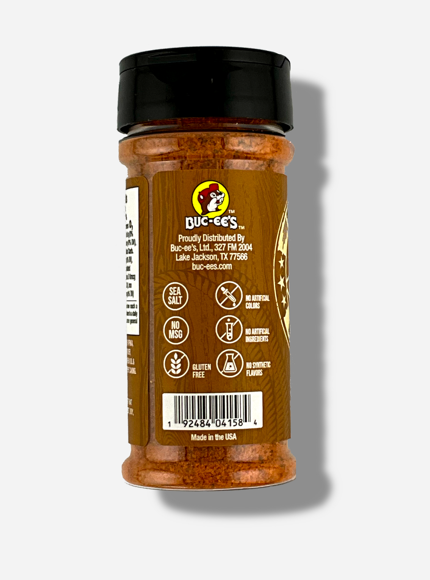 A picture of the side of a container of Texas Round Up Steak Seasoning. The container has a black plastic flip lid, and a clear plastic body.  The spices inside appear orange and black.  The tan label reads SEA SALT, NO MSG, GLUTEN FREE, NO ARTIFICIAL COLORS, NO ARTIFICIAL INGREDIENTS, NO SYNTHETIC FLAVORS.  Beneath that, MADE IN THE USA.