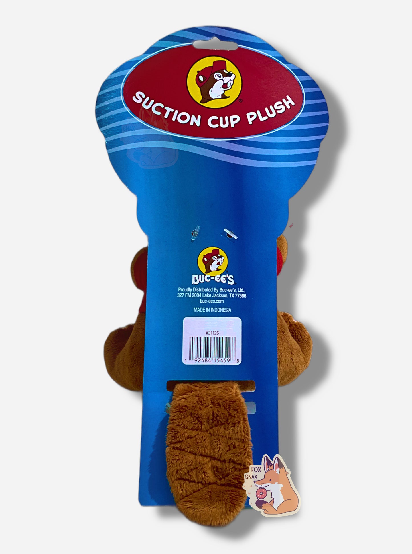 A picture of the back of a package of an adorable Buc-ee the Beaver plush.  Most of the view is a paper wrapper in blue and red that reads "Suction Cup Plush".  Buc-ee's brown-furred beaver tail can be seen poking out of the back of the package.