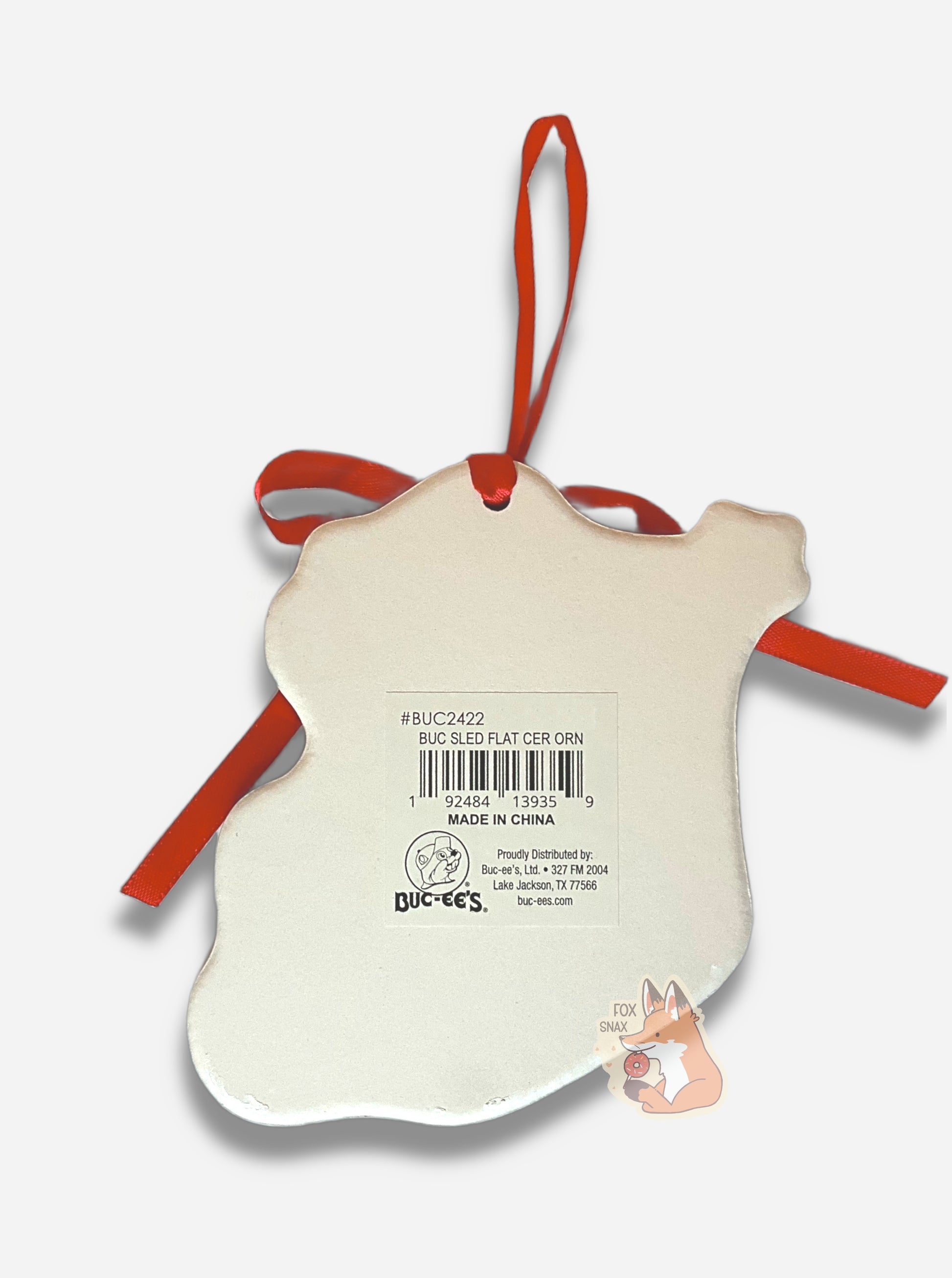 A picture of the back of a ceramic ornament, with a red ribbon at the top to hang it on a tree.  It is a shapeless flat white surface.