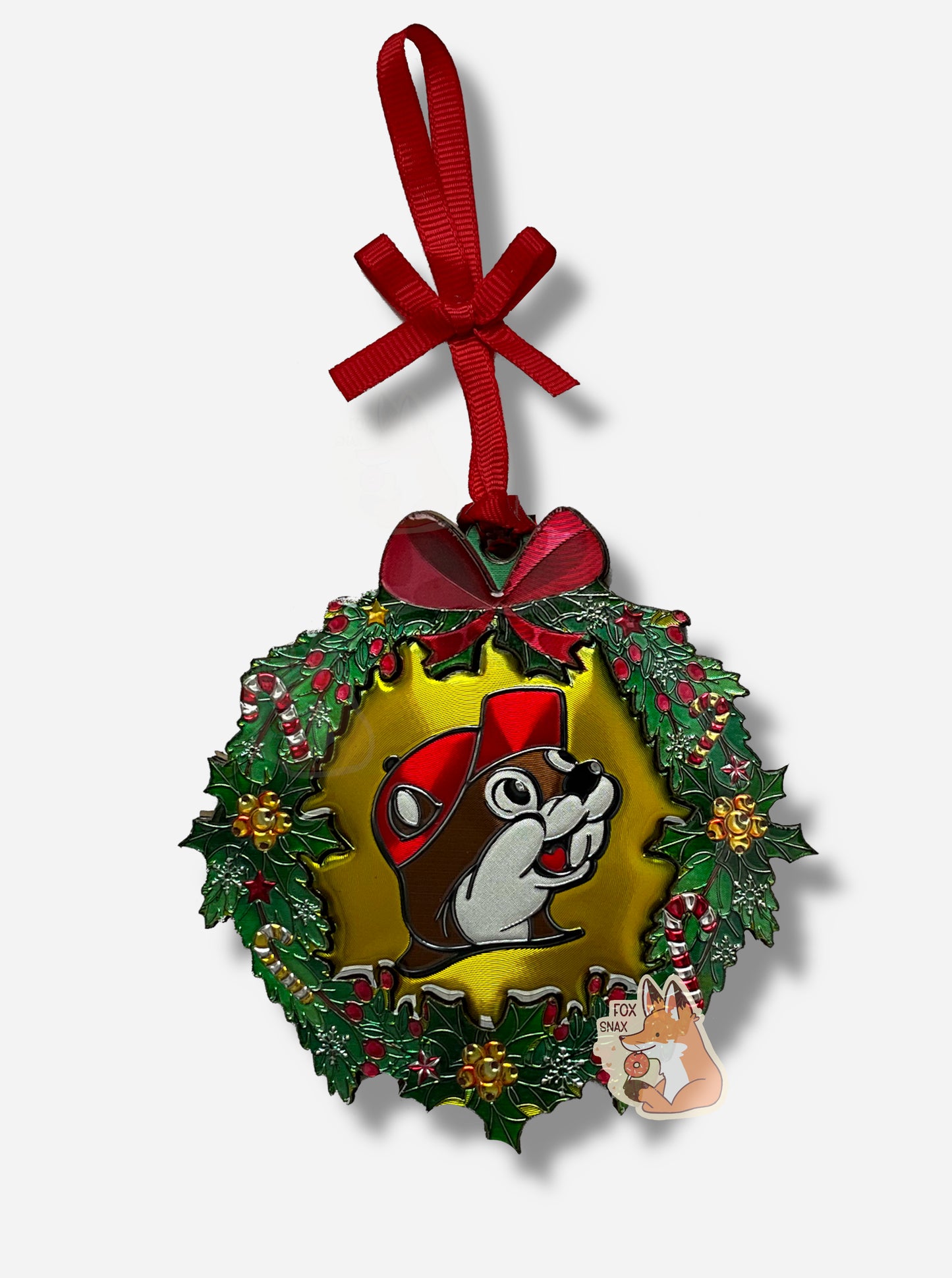 A picture of a circular ornament, in the shape of a green wreath.  The wreath is decorated with candy canes, holly berries, and yellow bells.  In the center of the ornament is the Buc-ee's logo (also in foil).  The top of the ornament has a foil red bow on it, and is tied to a red ribbon to attach to a tree.  