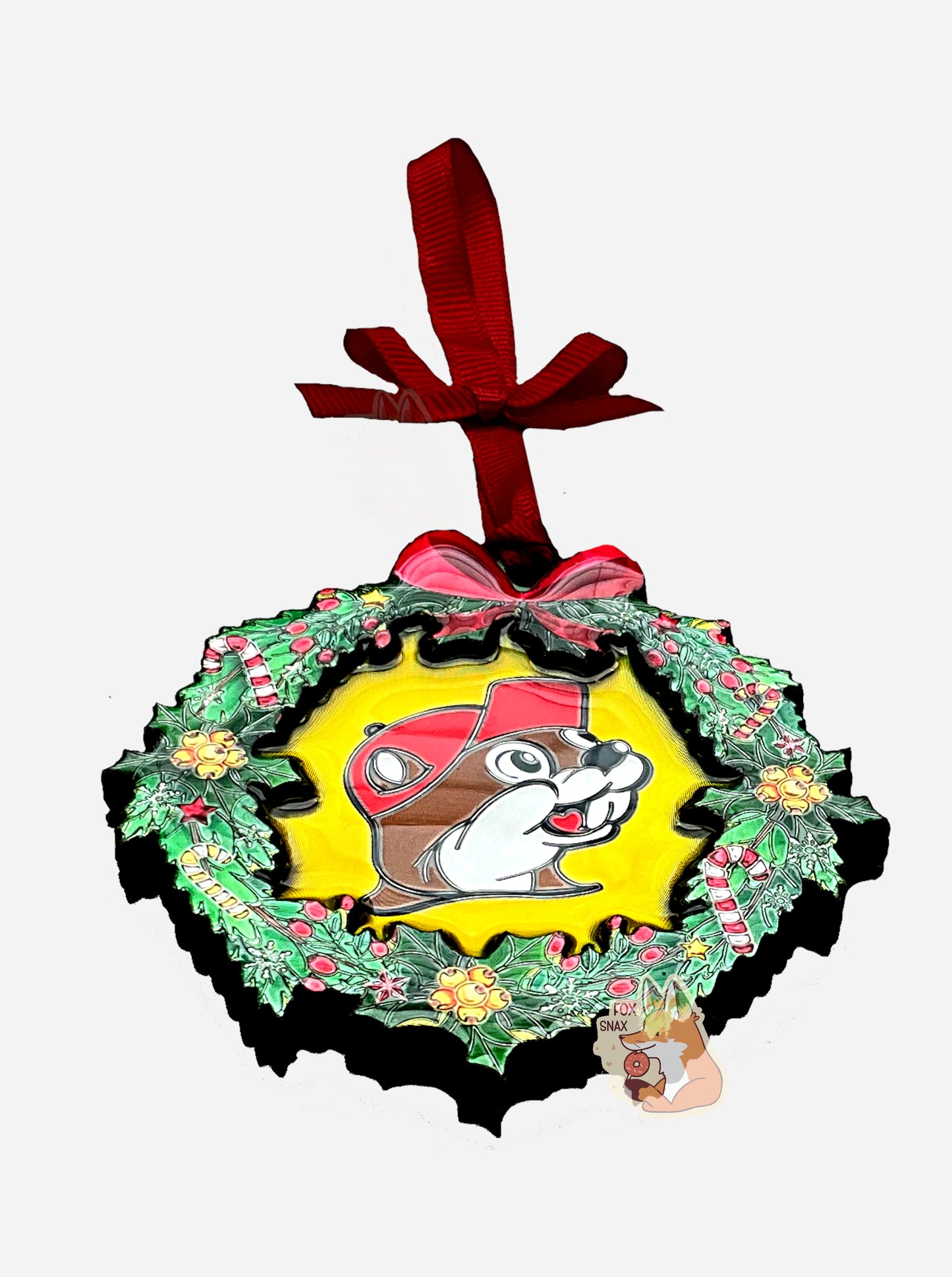 A picture of a circular ornament, in the shape of a green wreath.  The wreath is decorated with candy canes, holly berries, and yellow bells.  In the center of the ornament is the Buc-ee's logo (also in foil).  The top of the ornament has a foil red bow on it, and is tied to a red ribbon to attach to a tree.  The ornament is tilted into a three quarters view, showing that the wreath object has a bit of thickness to it.