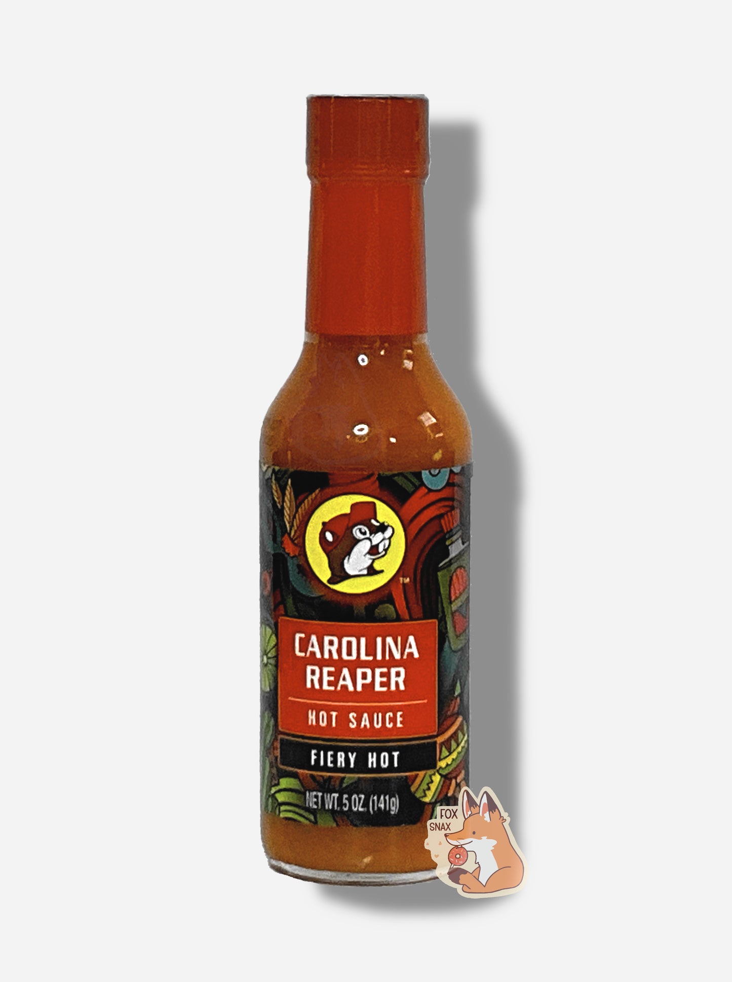 A picture of a small, tall glass bottle of hot sauce.  The top of the bottle is sealed with a red plastic cover on a black cap. The front label of the bottle reads CAROLINA REAPER HOT SAUCE, FIERY HOT.  The Buc-ee's logo can be seen on the front; the background is a fairly busy abstract artwork featuring a cactus, two maracas, a lime, and a Mardi Gras mask.  The sauce inside is red/orange.