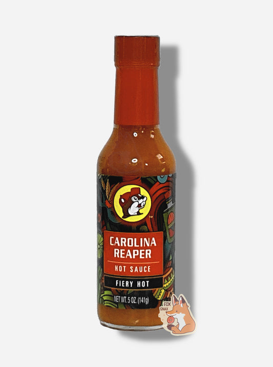 A picture of a small, tall glass bottle of hot sauce.  The top of the bottle is sealed with a red plastic cover on a black cap. The front label of the bottle reads CAROLINA REAPER HOT SAUCE, FIERY HOT.  The Buc-ee's logo can be seen on the front; the background is a fairly busy abstract artwork featuring a cactus, two maracas, a lime, and a Mardi Gras mask.  The sauce inside is red/orange.