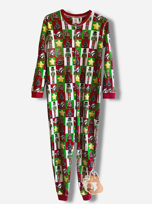 A picture of a large onesie that resembles Christmas wrapping.  Most of the wrapping is separated into squares or rectangles. The shapes have within them, alternately: yellow stars, Christmas trees, red wrapped presents with a pink bow, Buc-ee the Beaver dressed as a nutcracker with a green outfit.  The neck, sleeves, and ankles are in red.