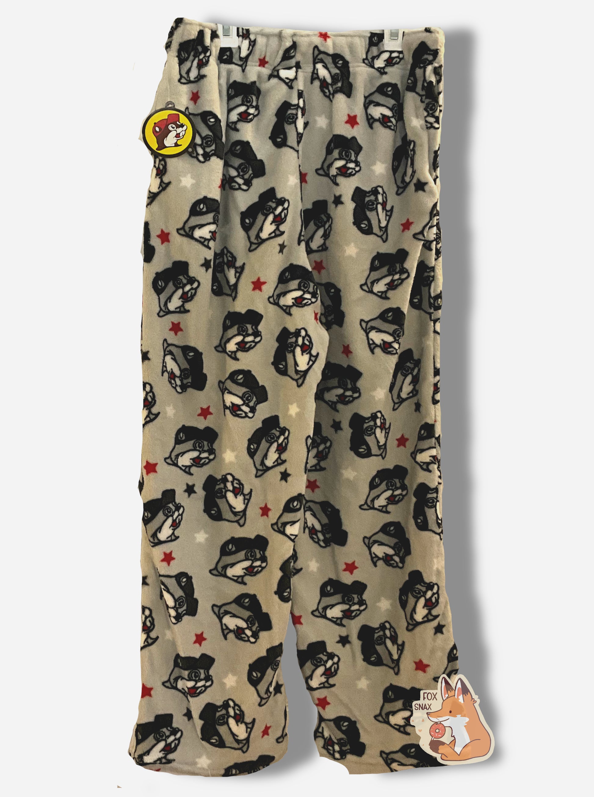 A picture of a pair of fuzzy lounge pants.  The pants are light grey and made of polyester.  The grey surface has tons of Buc-ee beaver heads on it, oriented different directions.  The surface also has red and white stars around the heads.  There is a drawstring to cinch the pants around one's waist, and it is made of a red cloth.  The edges are hemmed.  