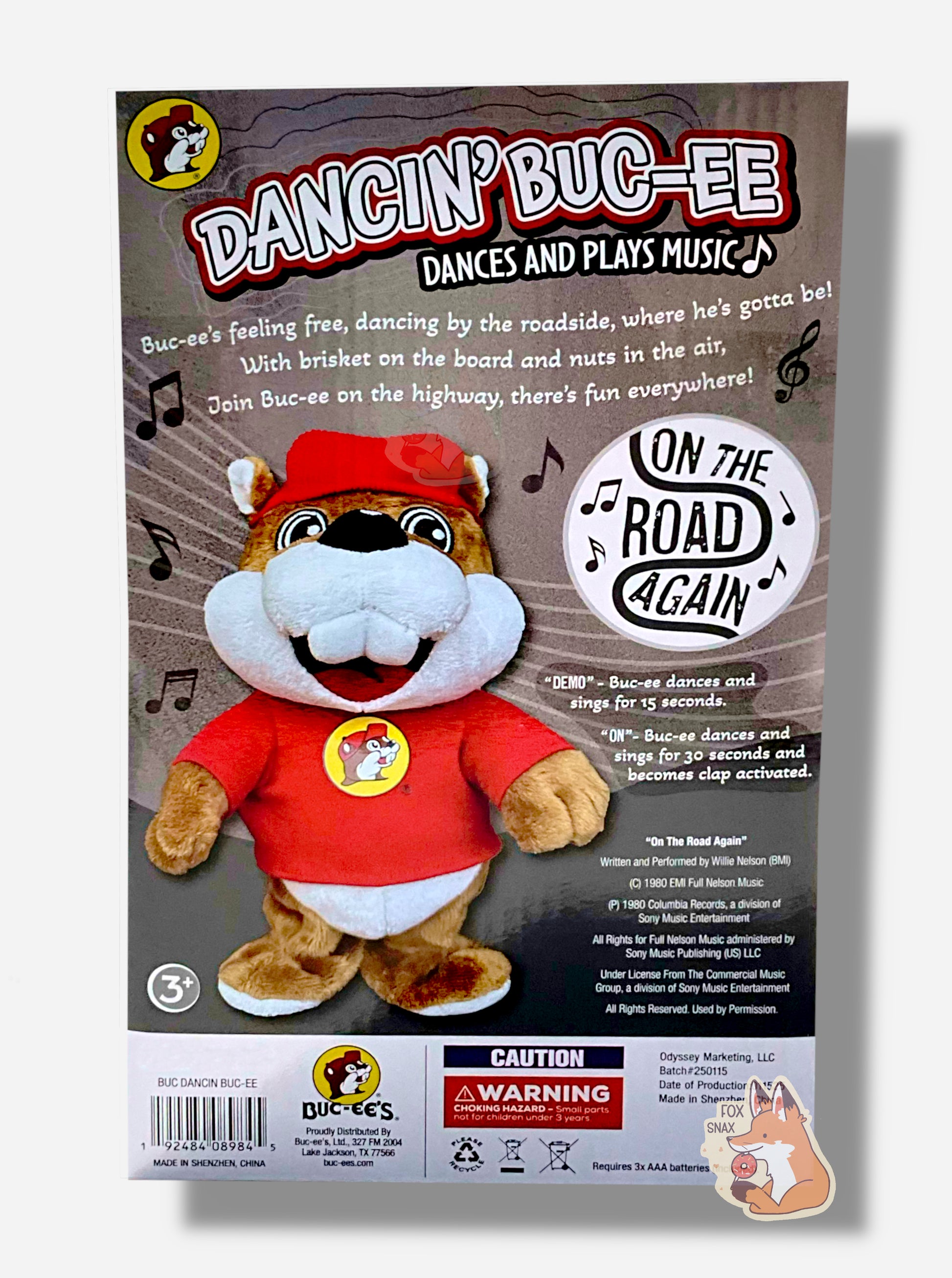 A picture of the back of a Dancin' Buc-ee package.  The package reads: "DANCIN BUC-EE DANCES AND PLAYS MUSIC.  Buc-ee's feeling free, dancing by the roadside, where he's gotta be!  With brisket on board and nuts in the air, Join Buc-ee on the highway, there's fun everywhere", then "ON THE ROAD AGAIN".  Next to the words is a picture of the Buc-ee animatronic.