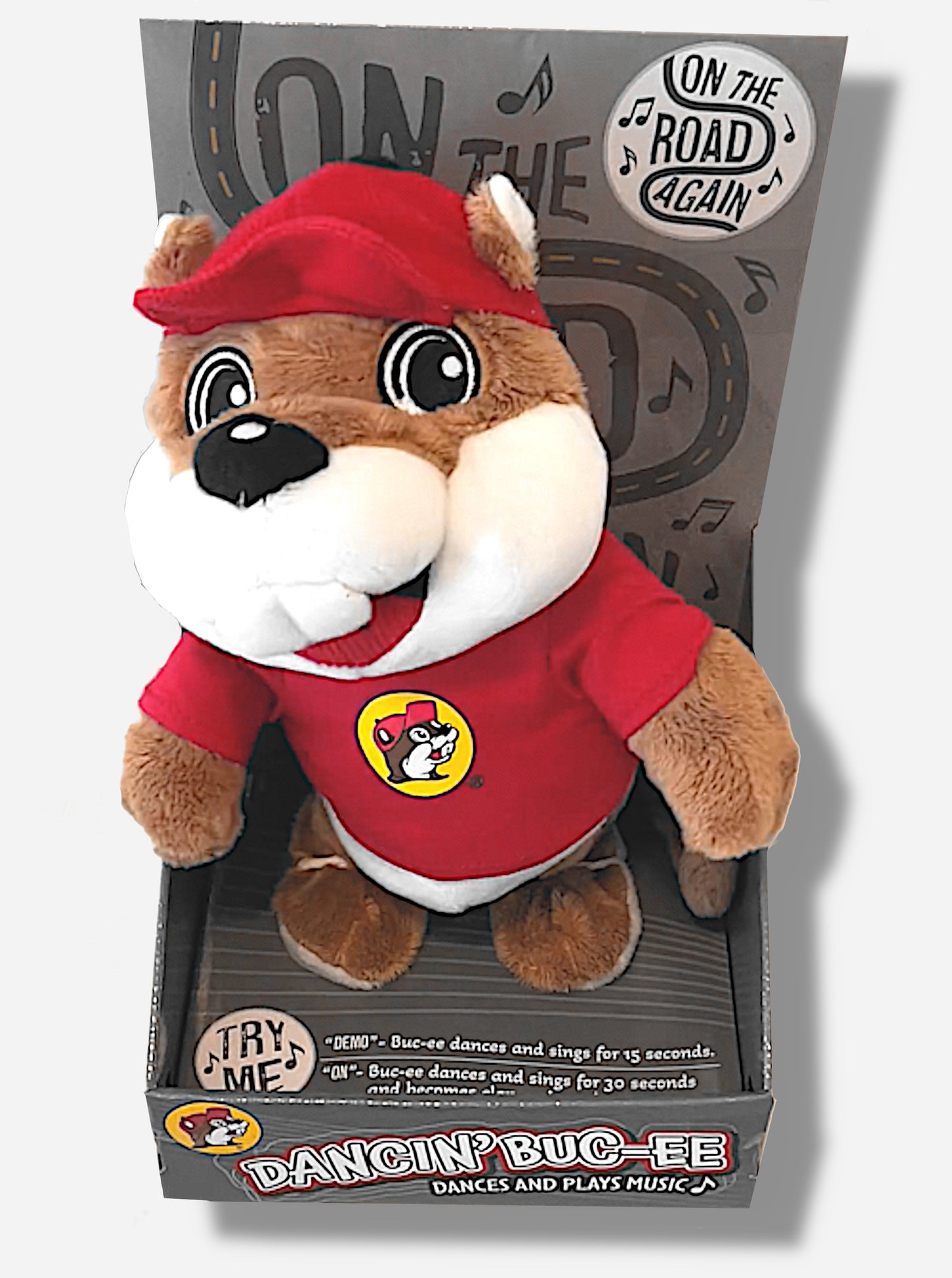 A picture of an adorable Buc-ee the Beaver plush.  The plush is of Dancin' Buc-ee, who is standing up on a grey product display.  He is wearing a red Buc-ee's shirt and red ball cap, and is looking at the viewer.  Buc-ee's is covered plush brown and white stuffed animal "fur".  Behind him the text reads "ON THE ROAD AGAIN", then "DANCIN' BUC-EE DANCES AND PLAYS MUSIC", then "DEMO- Buc-ee dances and sings for 15 seconds", "ON-Buc-ee dances and sings for 30 seconds"