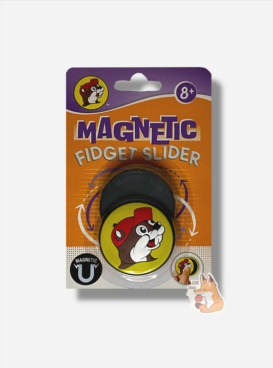 A picture of a rectangular package of Buc-ee's Magnetic Fidget Sliders.  The package is in purple at the top, then orange in the middle, then white at the bottom with orange dots.  The top reads 8+, then MAGNETIC FIDGET SLIDER, then MAGNETIC at the bottom with a small U-shaped magnet.  In the middle are a pair of circular magnetic fidget sliders with the Buc-ee's logo on them.