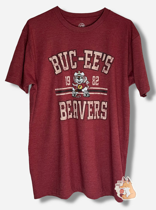 A picture of the front of a red t-shirt.  The shirt has text on the top that reads BUC-EE'S, and text on the bottom reading BEAVERS.  In the middle of the words are a picture of Buc-ee the Beaver wearing a dark red football uniform, complete with helmet.  On either side of Buc-ee are the numbers 19 and 82.