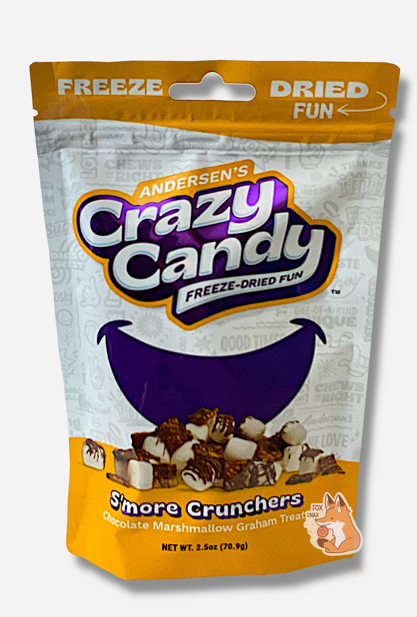 A large bag of Andersen's S'more Crunchers.  The front of the bag also says Chocolate Marshmallow Graham Treats, Net Weight 2.5 oz.  It's Fun, Happy, Candy.  The top and bottom of the bag are yellow, and the background is a large purple smile against a white background.