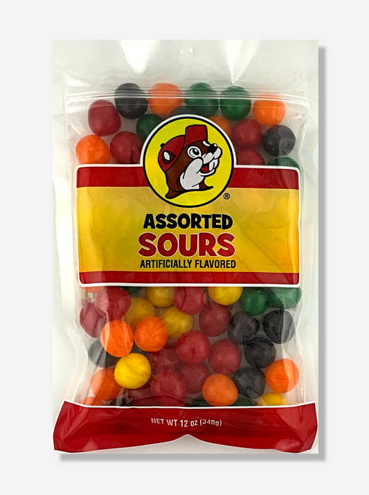 A picture of the front of a resealable bag of Buc-ee's Assorted Sours, which are sour and sweet candies.  The bag reads ASSORTED SOURS, Artificially Flavored, and has a picture of Buc-ee the Beaver on it.  The sours inside are round, and are multiple shades of red, orange, yellow, green, and purple.