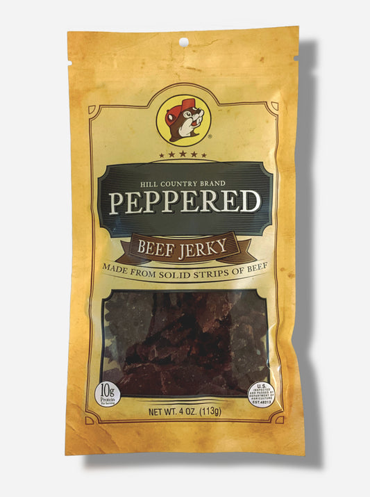 A picture of the front of a tan plastic bag of Buc-ee's Hill Country Brand Peppered Beef Jerky.  The logo is in dark grey with white text.  The label underneath reads 'Made From Solid Strips Of Beef'.A small window on the bottom of the bag shows the dark brown/red dried jerky inside.  The bag has a picture of Buc-ee the Beaver on it.