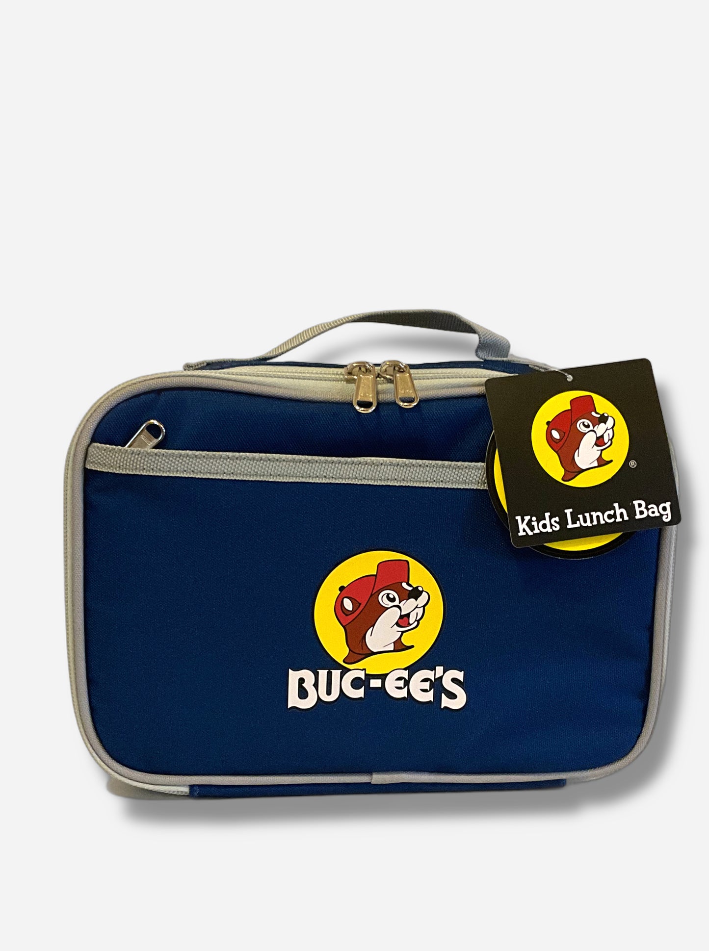 A picture of a front view of a children's lunch box.  The outer surface is made of blue polyester, and has a small tan strap on the top.  The front of the cooler has a picture of the Buc-ee's logo on it: a grinning beaver wearing a red hat against the background of a yellow circle.  Underneath the logo reads BUC-EE'S in white text. The front of the lunch box has a small zip pocket.  The top right of the lunch box has a paper tag that reads KIDS LUNCH BAG.