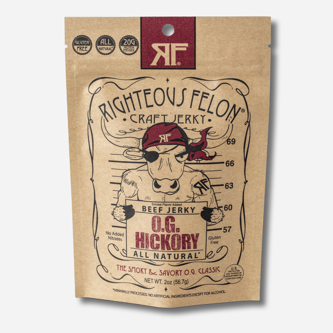 A picture of the front of a kraft paper bag of Righteous Felon O.G. Hickory Beef Jerky with a maroon RF logo at the top.  Badges in the corner read "Gluten Free", "All Natural", and "20g Protein per Pack".  Below the Righteous Felon Craft Jerky text, a cartoon bull in a maroon bandana and eye patch poses for a mugshot in front of a height chart, holding a sign that reads "Beef Jerky, O.G. Hickory, All Natural".  At the bottom it reads "The Smoky & Savory O.G. Classic" and "Net Wt. 2oz (56.7g)".