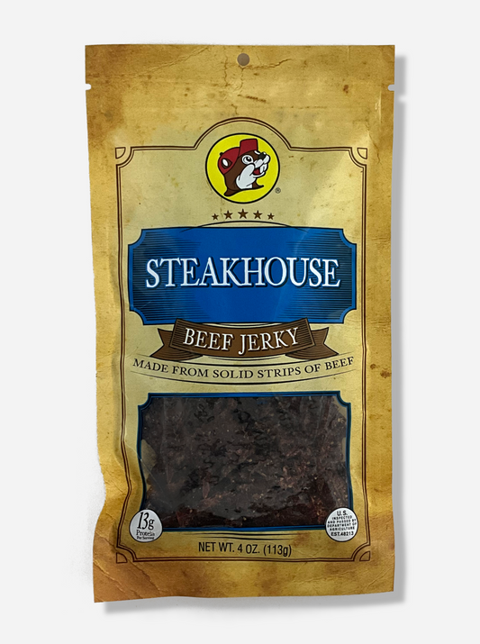 A picture of the front of a tan plastic bag of Buc-ee's Steakhouse Beef Jerky.  The logo is in dark blue with white text.  The label underneath reads 'Made From Solid Strips Of Beef'.A small window on the bottom of the bag shows the dark brown/red dried jerky inside.  The bag has a picture of Buc-ee the Beaver on it.