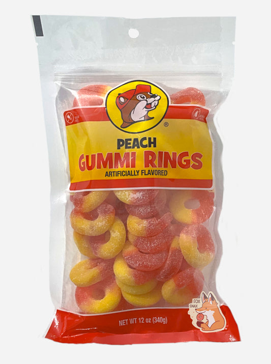 A picture of a clear plastic bag of Buc-ee's Peach Rings.  The bag reads ARTIFICIALLY FLAVORED, then NET WT 12 OZ (340 g).  Inside the bag, gummi peach rings can be seen; they are half red and half orange.