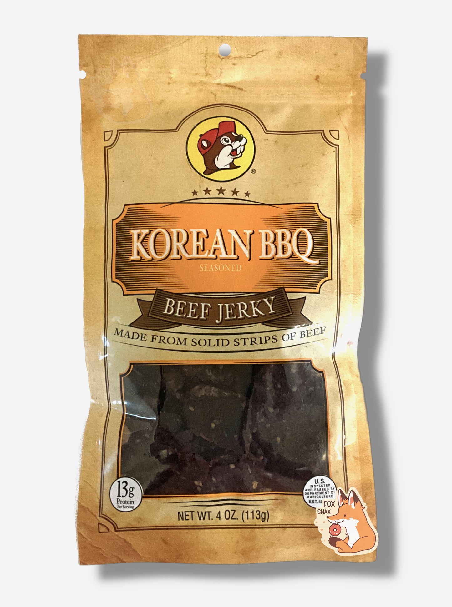 A picture of the front of a tan plastic bag of Buc-ee's Korean BBQ Beef Jerky.  The logo is in orange with white text.The label underneath reads 'Made From Solid Strips Of Beef'.A small window on the bottom of the bag shows the dark brown dried jerky inside.  The bag has a picture of Buc-ee the Beaver on it.