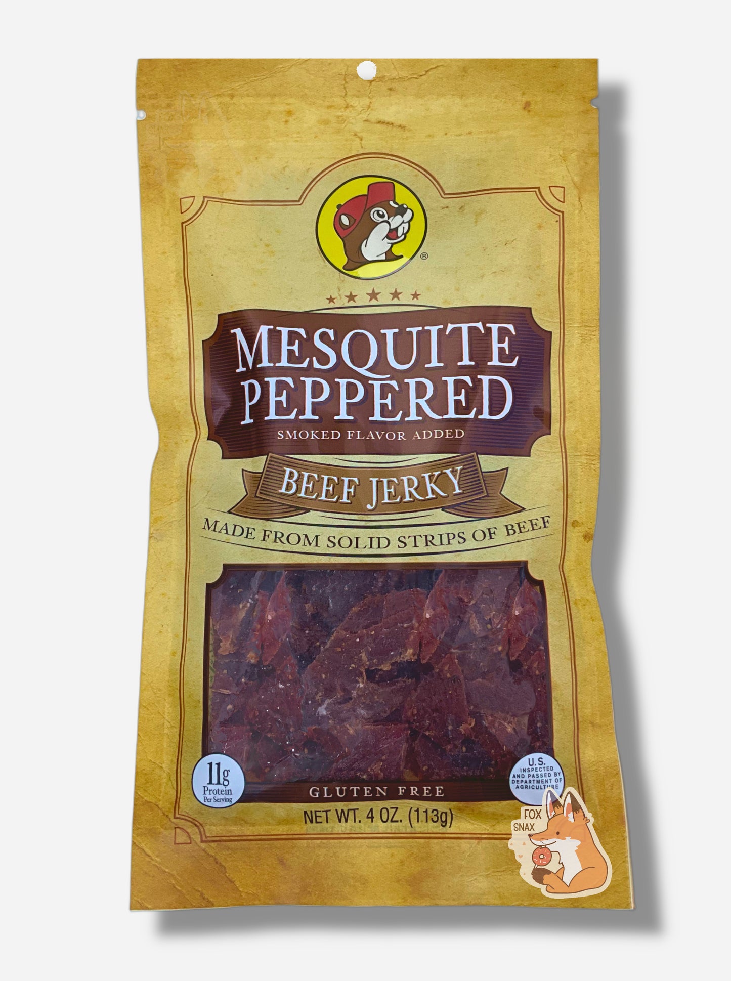A picture of the front of a tan plastic bag of Buc-ee's Mesquite Peppered Jerky.  The logo is in brown with white text.The label underneath reads 'Smoked Flavor Added', then 'Beef Jerky', then 'Made From Solid Strips Of Beef'. A small window on the bottom of the bag shows the dark brown/red dried jerky inside.  The bag has a picture of Buc-ee the Beaver on it.