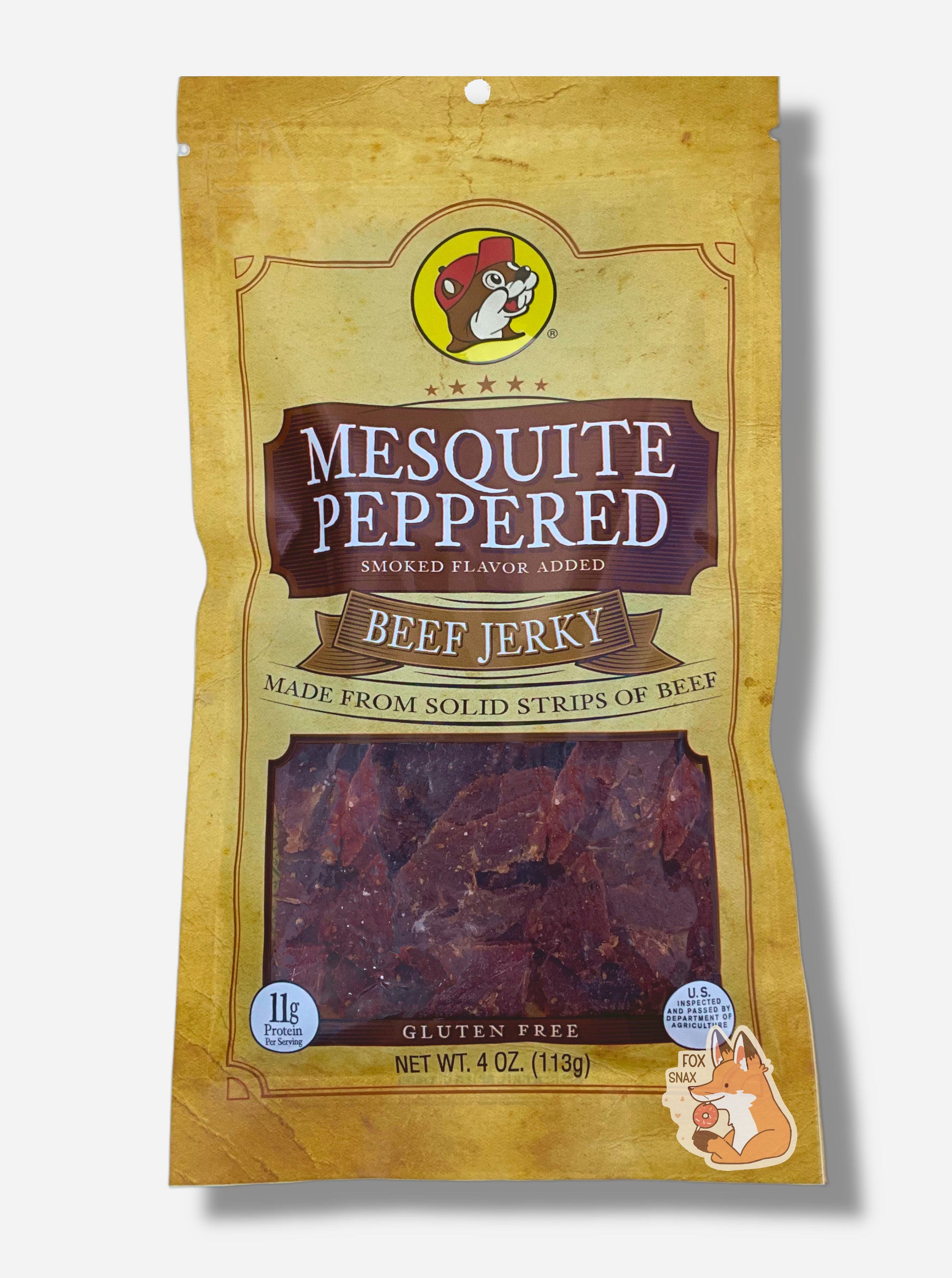 A picture of the front of a tan plastic bag of Buc-ee's Mesquite Peppered Jerky.  The logo is in brown with white text.The label underneath reads 'Smoked Flavor Added', then 'Beef Jerky', then 'Made From Solid Strips Of Beef'. A small window on the bottom of the bag shows the dark brown/red dried jerky inside.  The bag has a picture of Buc-ee the Beaver on it.