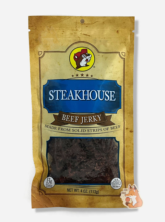 A picture of the front of a tan plastic bag of Buc-ee's Steakhouse Beef Jerky.  The logo is in dark blue with white text.  The label underneath reads 'Made From Solid Strips Of Beef'.A small window on the bottom of the bag shows the dark brown/red dried jerky inside.  The bag has a picture of Buc-ee the Beaver on it.