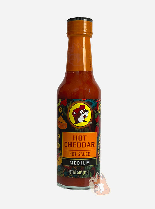 A picture of a small, tall glass bottle of hot sauce.  The top of the bottle is sealed with a orange plastic cover on a black cap.  The front label of the bottle reads HOT CHEDDAR, HOT SAUCE, MEDIUMN.  The Buc-ee's logo can be seen on the front; the background is a fairly busy abstract artwork featuring chilis, maracas, aztec wheels, and cheese wedges. The sauce inside is a orange/red.