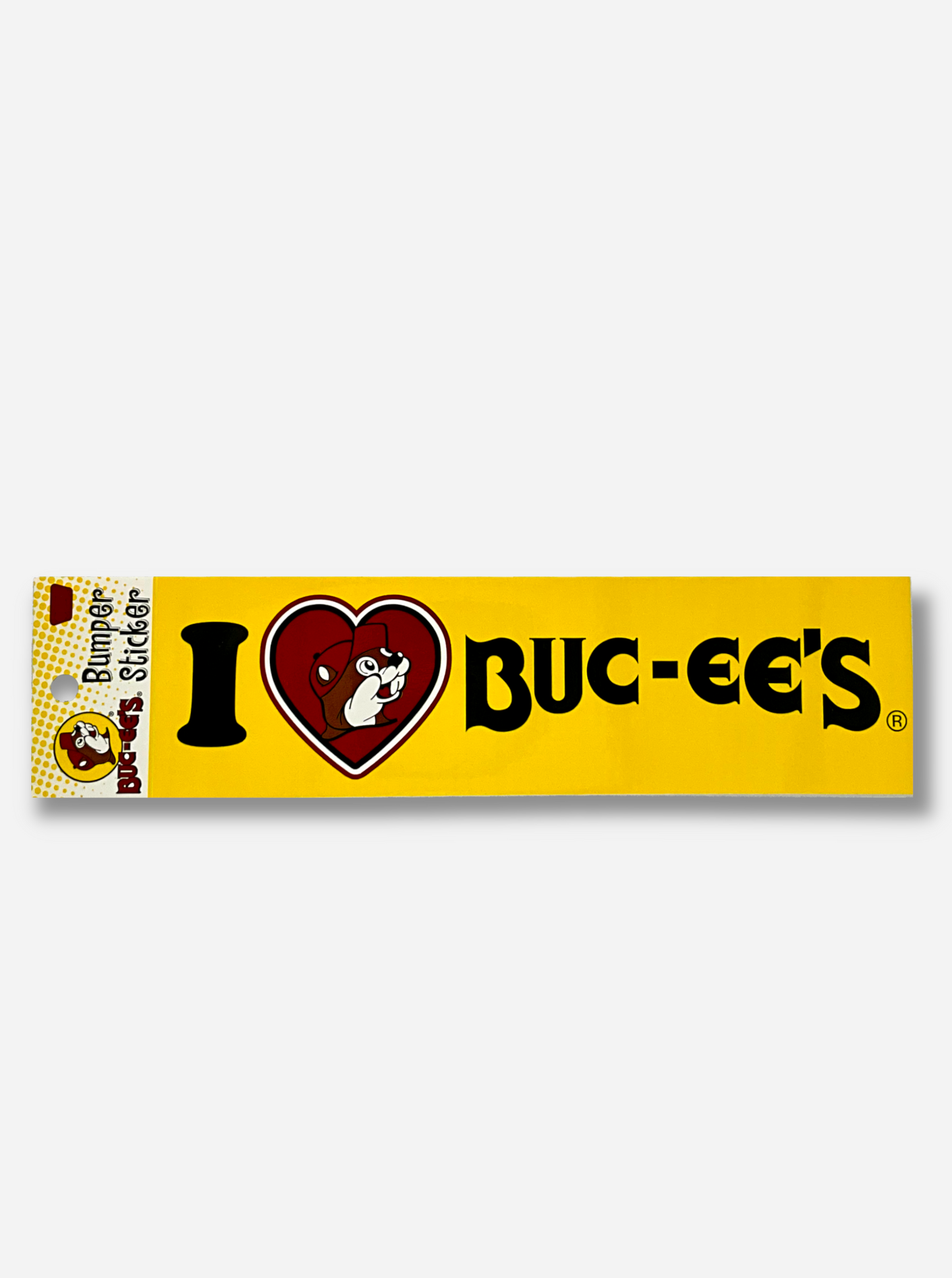 A picture of a bumper sticker.  It has a yellow background, and black text, and says I <heart> BUC-EE'S across its face.  However, inside the heart, which is colored red, is a white outline, then black outline, then a red background with Buc-ee The Beaver, wearing his red ball cap.  The packaging reads BUC-EE'S BUMPER STICKER.