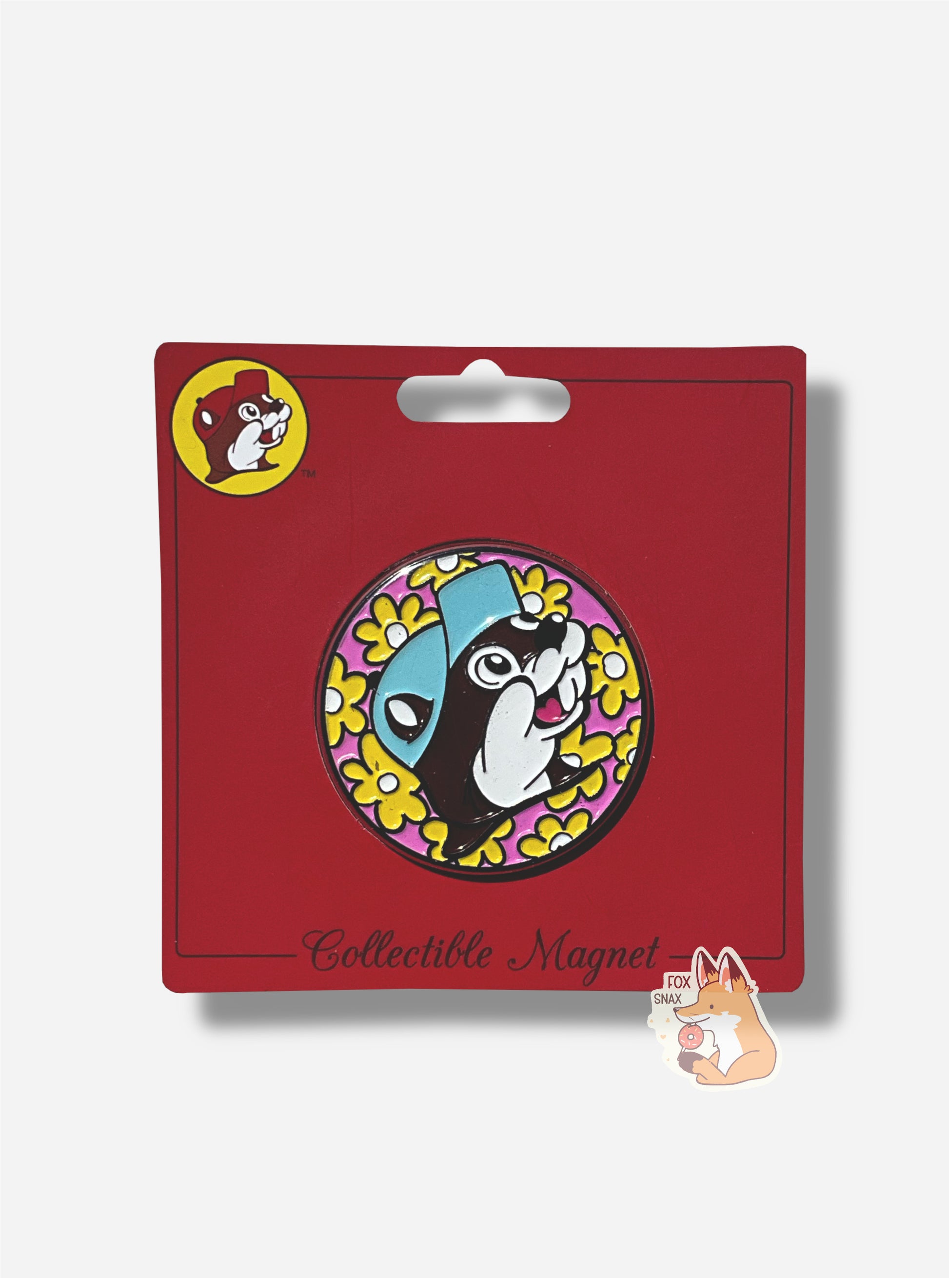 A picture of the front of plastic collectible magnet.  The magnet  is a circle, which contains the Buc-ee's logo - a cheerful beaver wearing a light blue ball cap, in front of a pink circle logo.  The pink circle is framed with yellow cartoon flowers with a white center.  The entire magnet has a paper backing; the backing is in red and reads in a fancy black font, 'Collectible Magnet'.