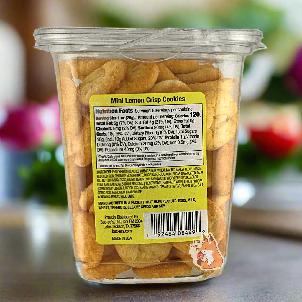 The back of a clear plastic, tall, rectangular package of Buc-ee's Mini Lemon Crisp Cookies.  The back label reads Manufactured in a facility that uses Peanuts, Eggs, Milk, Wheat, Treenuts, Sesame Seeds and Soy. The background is of a cheery kitchen with a grey marble countertop, with flowers in the background.