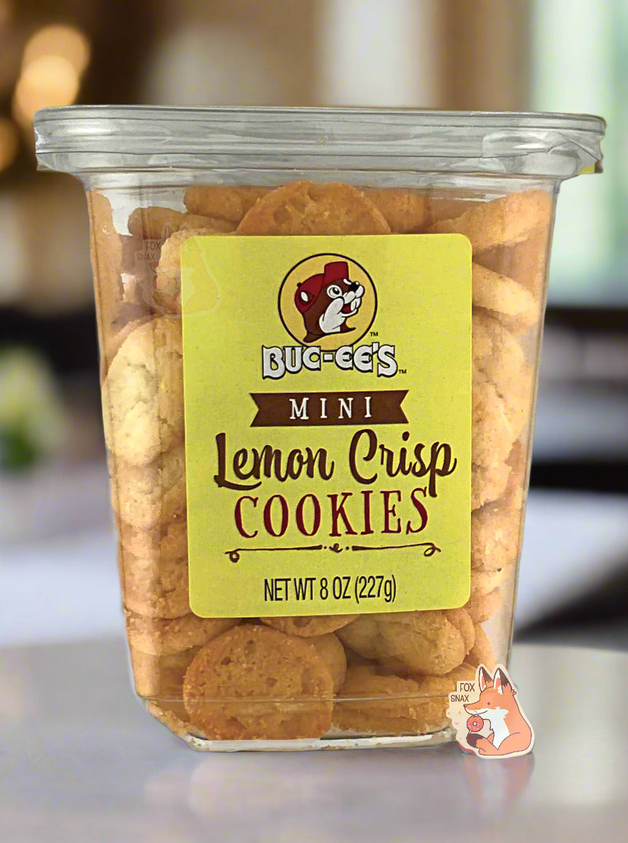 The front of a clear plastic, tall, rectangular package of Buc-ee's Mini Lemon Crisp Cookies.  The label has a small logo of Buc-ee The Beaver on it with a bright yellow cheery background.  The background is of a cheery kitchen with a white marble countertop.