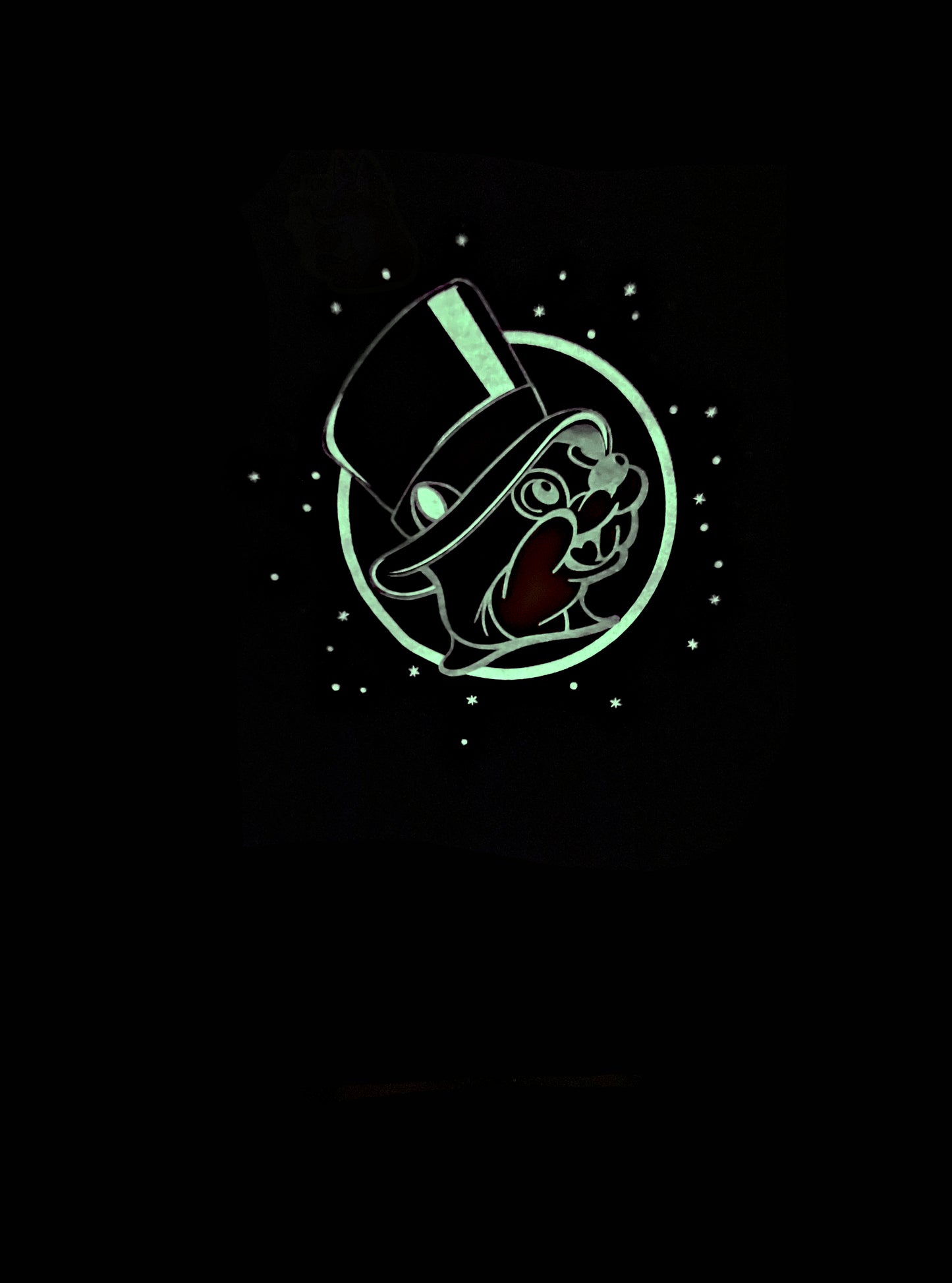 A picture of a glowing green logo on a glow in the dark t-shirt.  The center of the t-shirt is the Buc-ee's logo, but Buc-ee is wearing a black top hat instead of his usual red ball cap.  Surrounding the logo is a series of glowing green dots and stars.