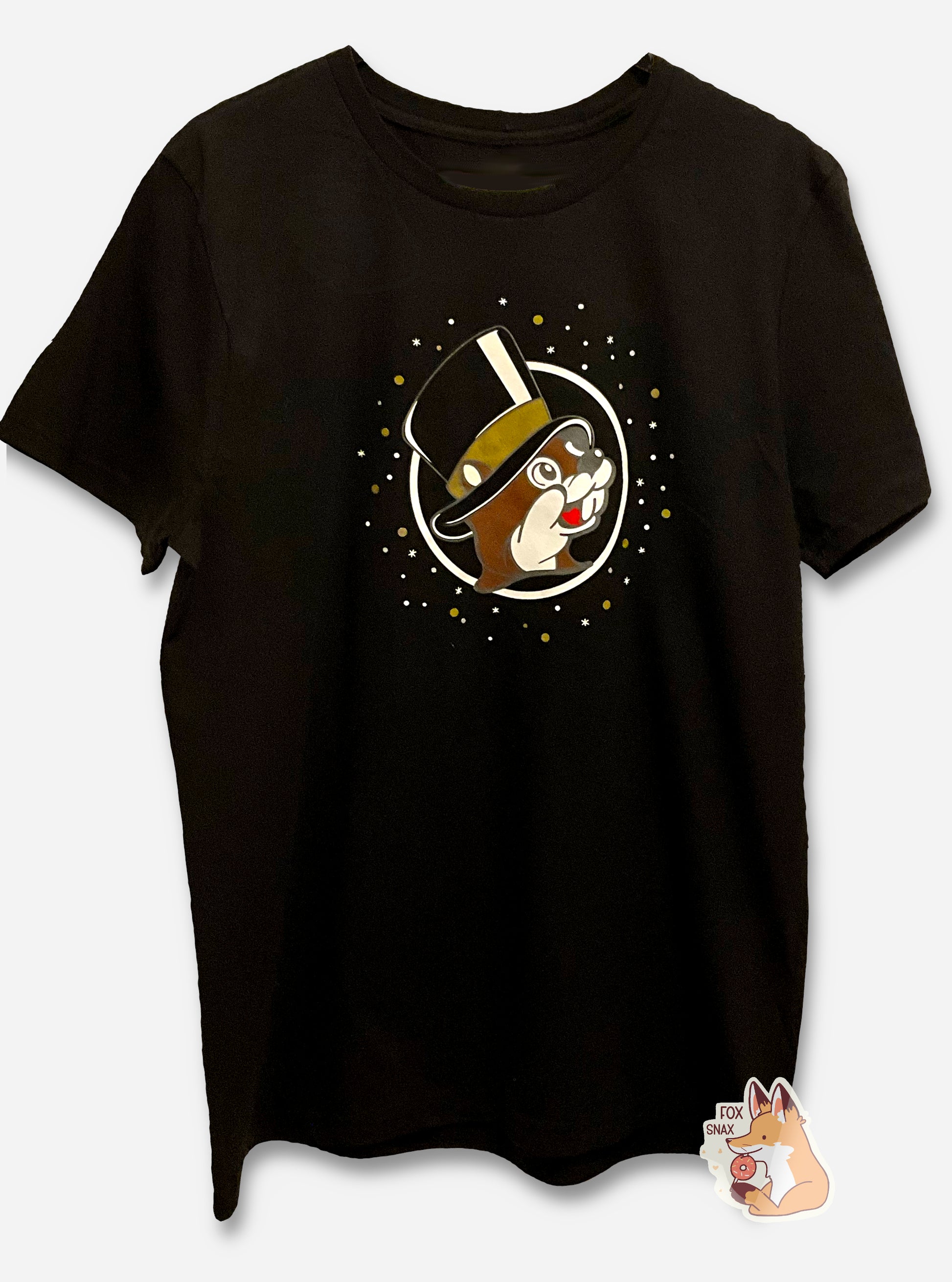 A picture of a black t-shirt.  The center of the t-shirt is the Buc-ee's logo, but Buc-ee is wearing a black top hat, with a gold band, instead of his usual red ball cap.  Surrounding the logo is a series of gold and silver dots and stars.